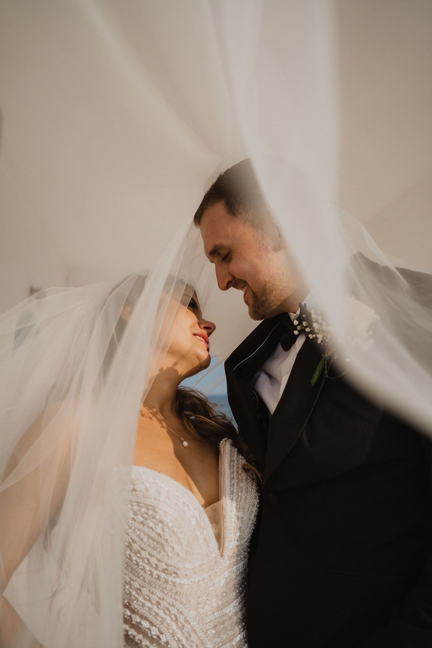 Romantic close-up of bride and groom almost kissing under a flowing white wedding veil.