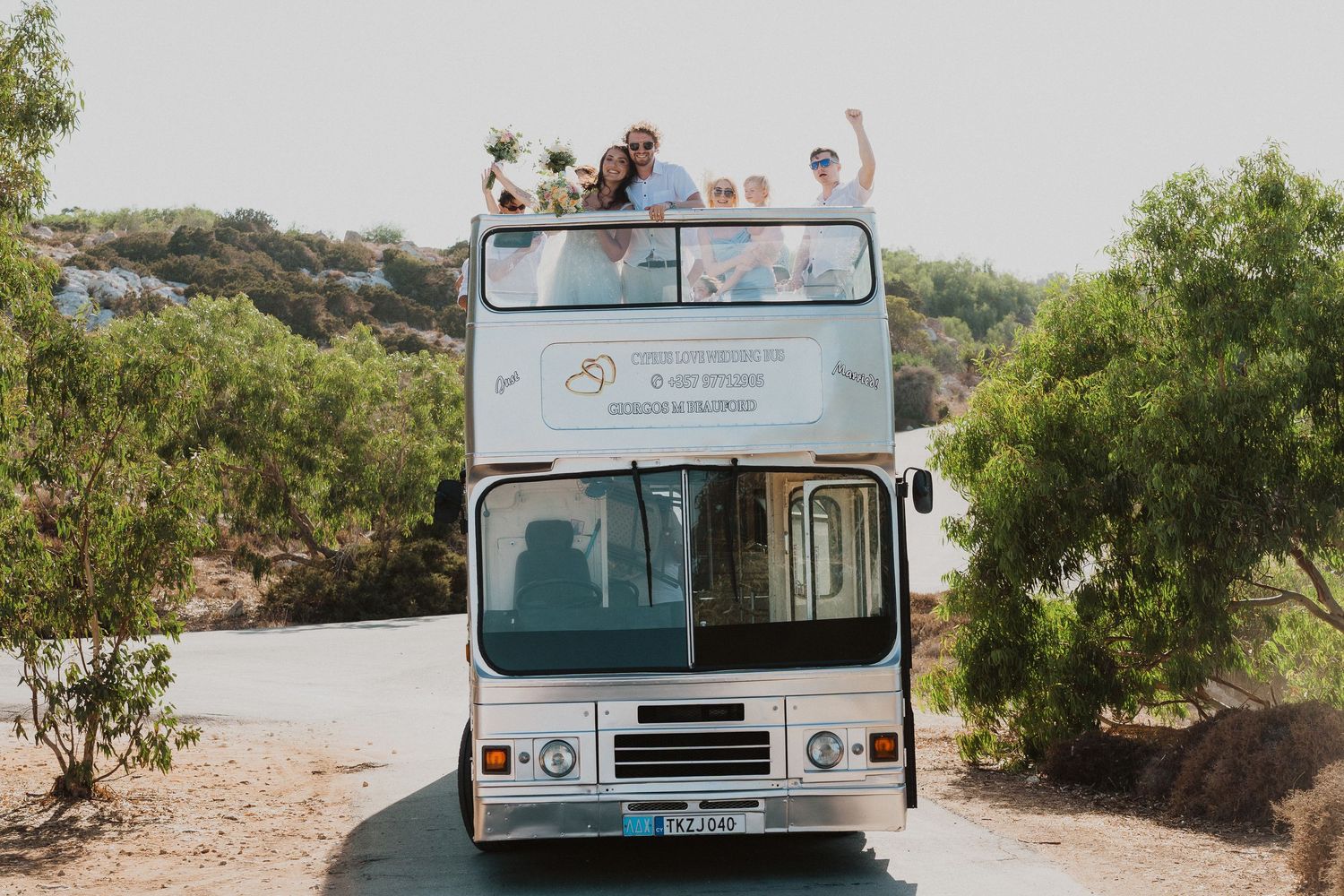 Light blue double decker wedding bus parked in a scenic location surrounded by trees and hills.
