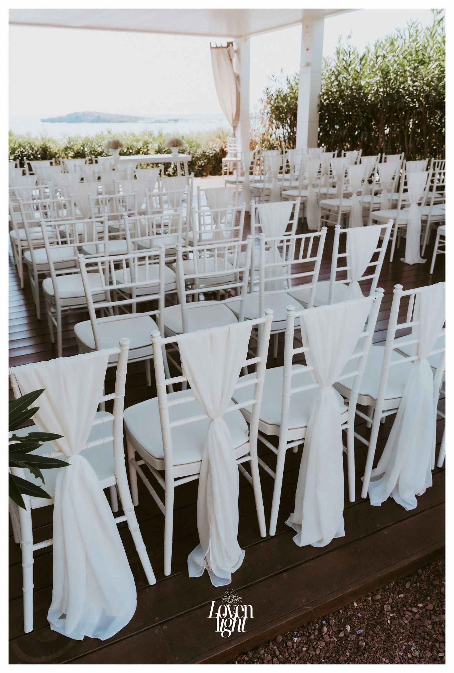 White chiavari chairs with flowing fabric drapes arranged for an outdoor wedding ceremony.