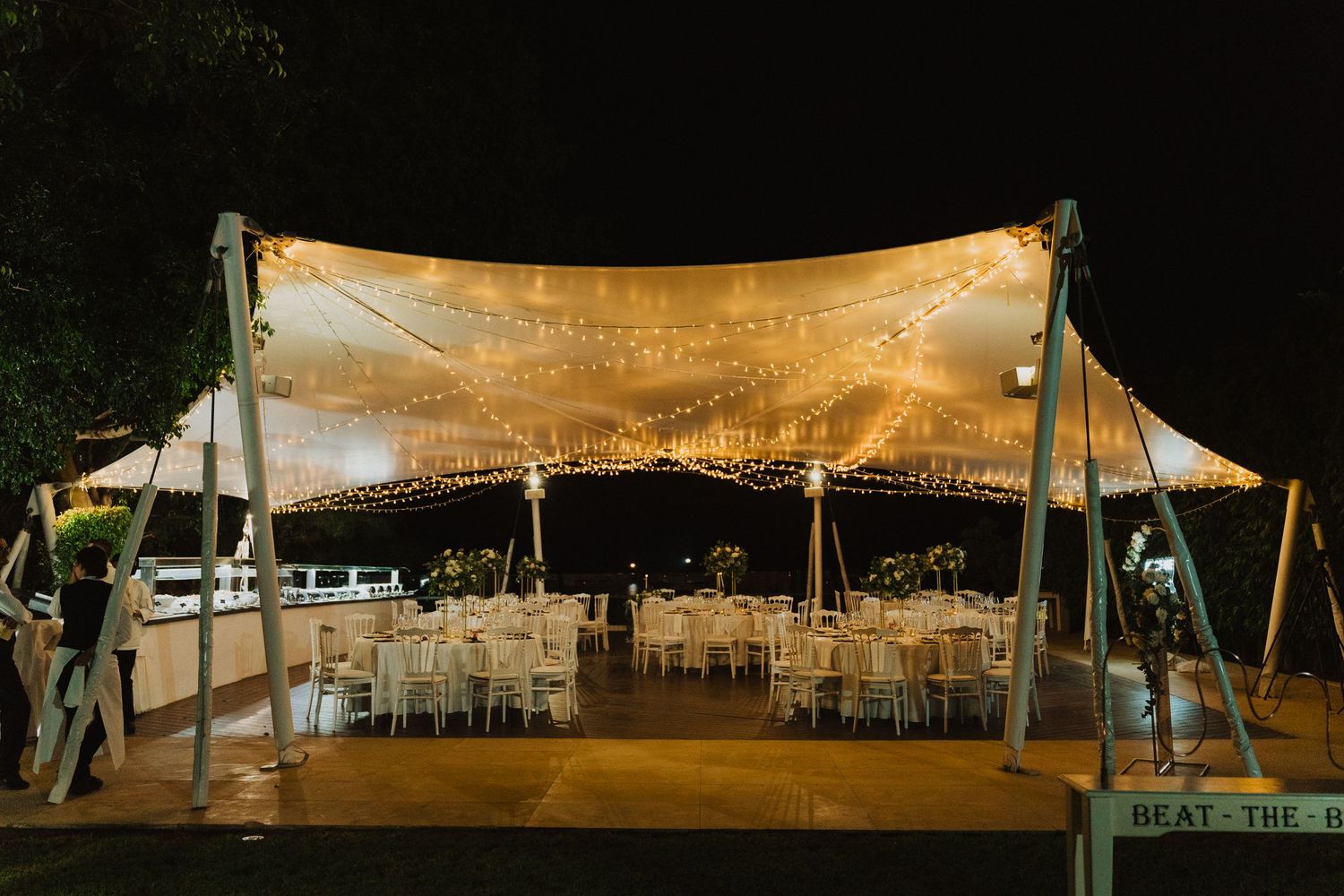 Elegant outdoor wedding tent with string lights and white fabric canopy glowing warmly at night.