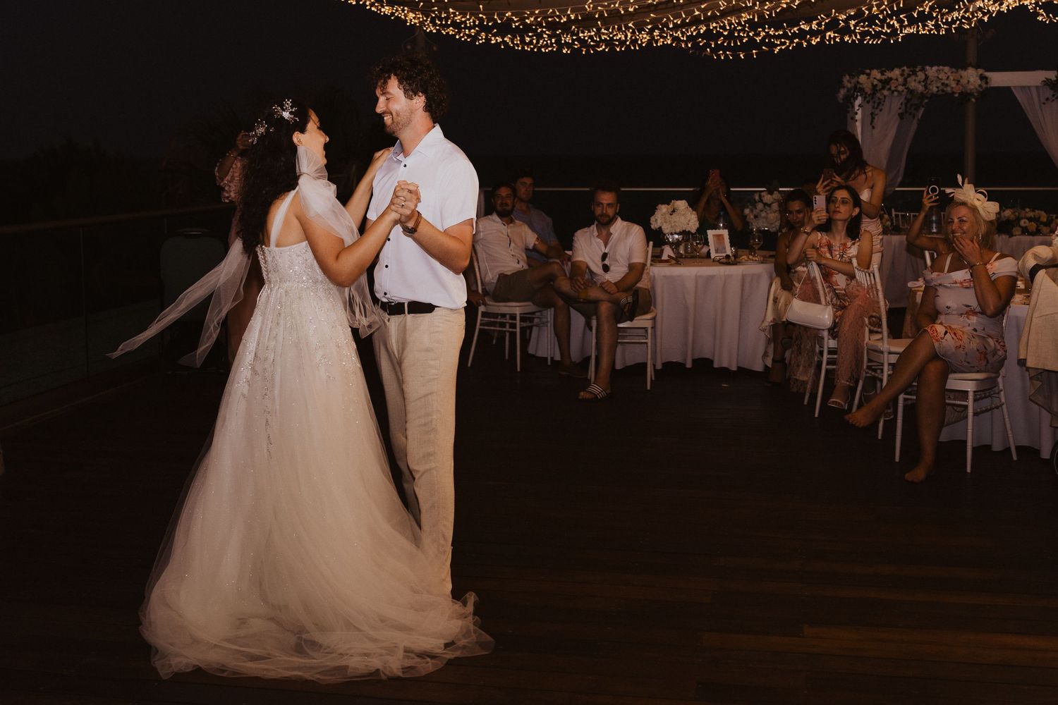 Newlyweds share their first dance under romantic string lights at an outdoor reception.