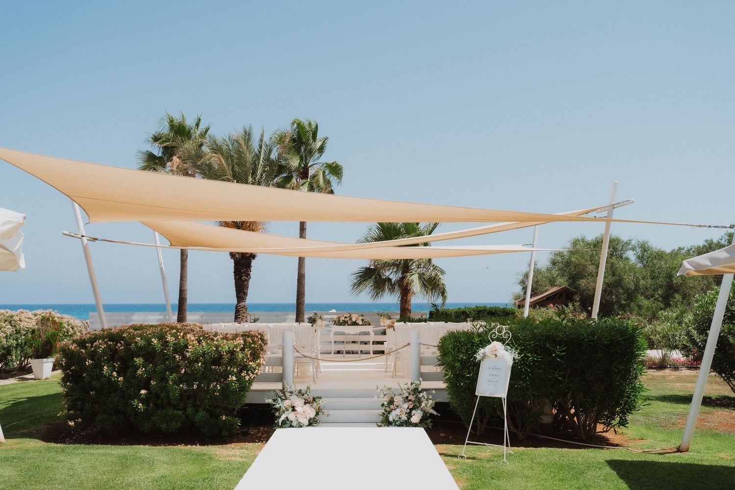 Outdoor wedding ceremony space with white aisle runner and beige canopies against a seaside backdrop.