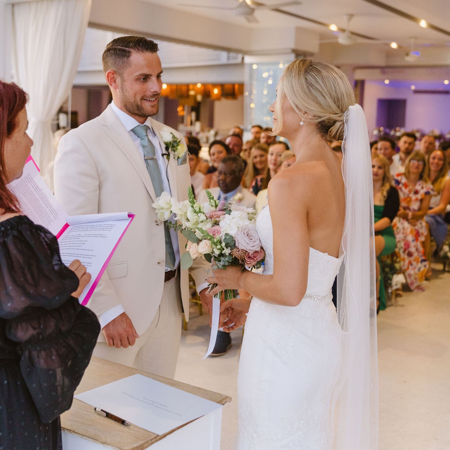 Indoor wedding ceremony with couple exchanging vows in front of gathered guests.