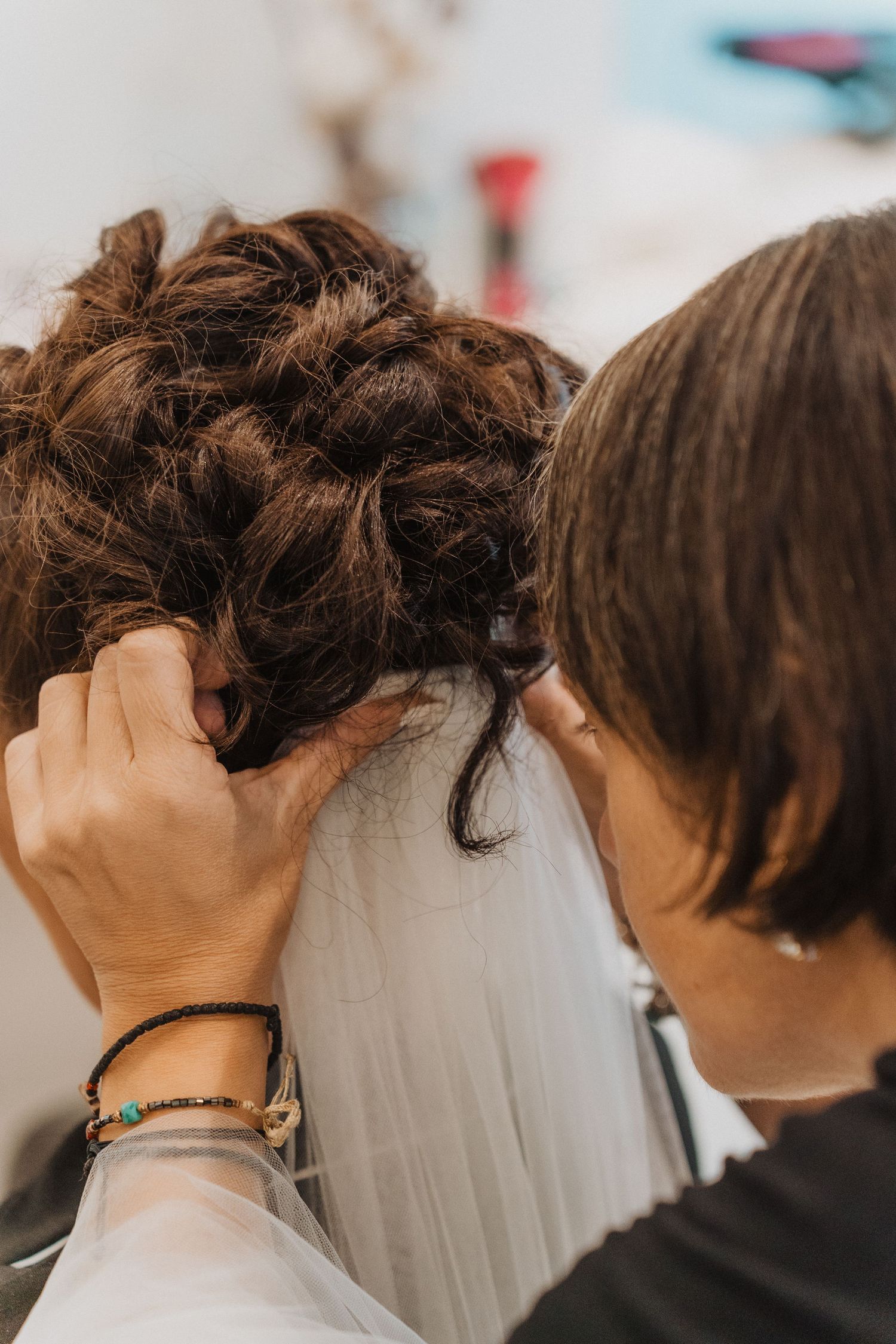 A hairstylist arranges an intricate updo with a white veil for a wedding day preparation.