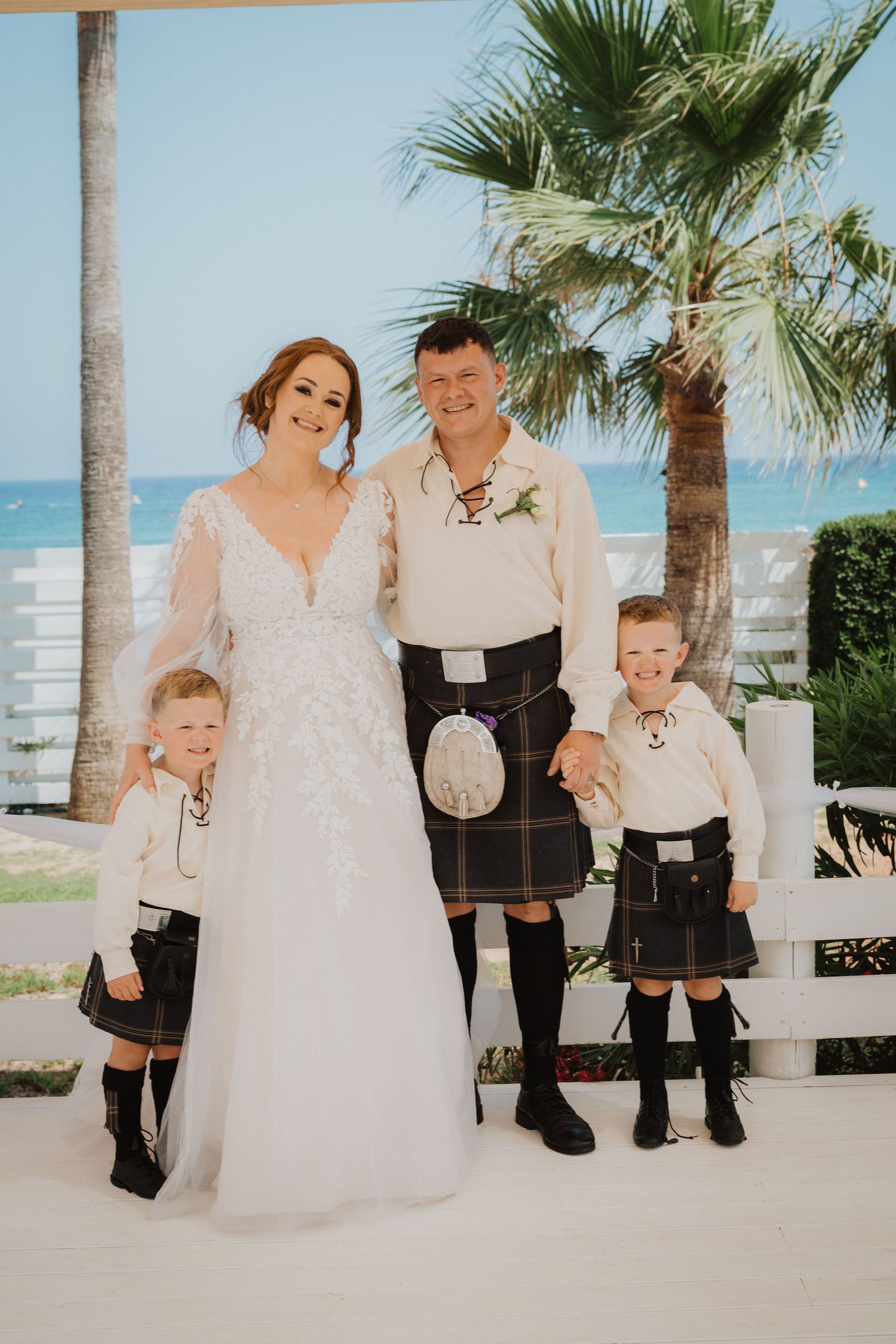 Scottish-themed family portrait with traditional kilts against a tropical beachside backdrop.