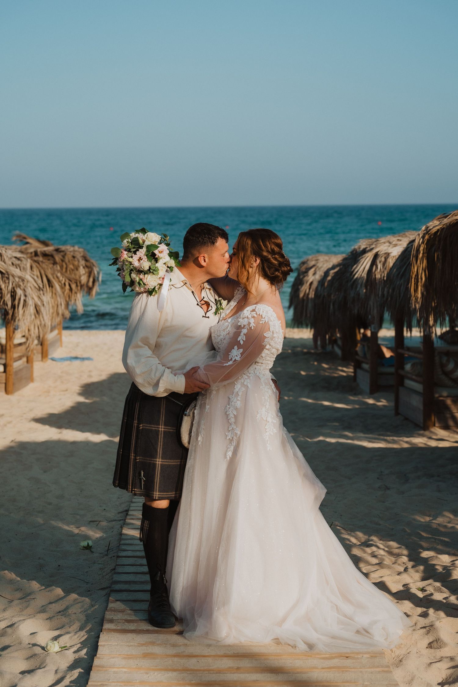Couple sharing a romantic moment on a wooden boardwalk with beach umbrellas.