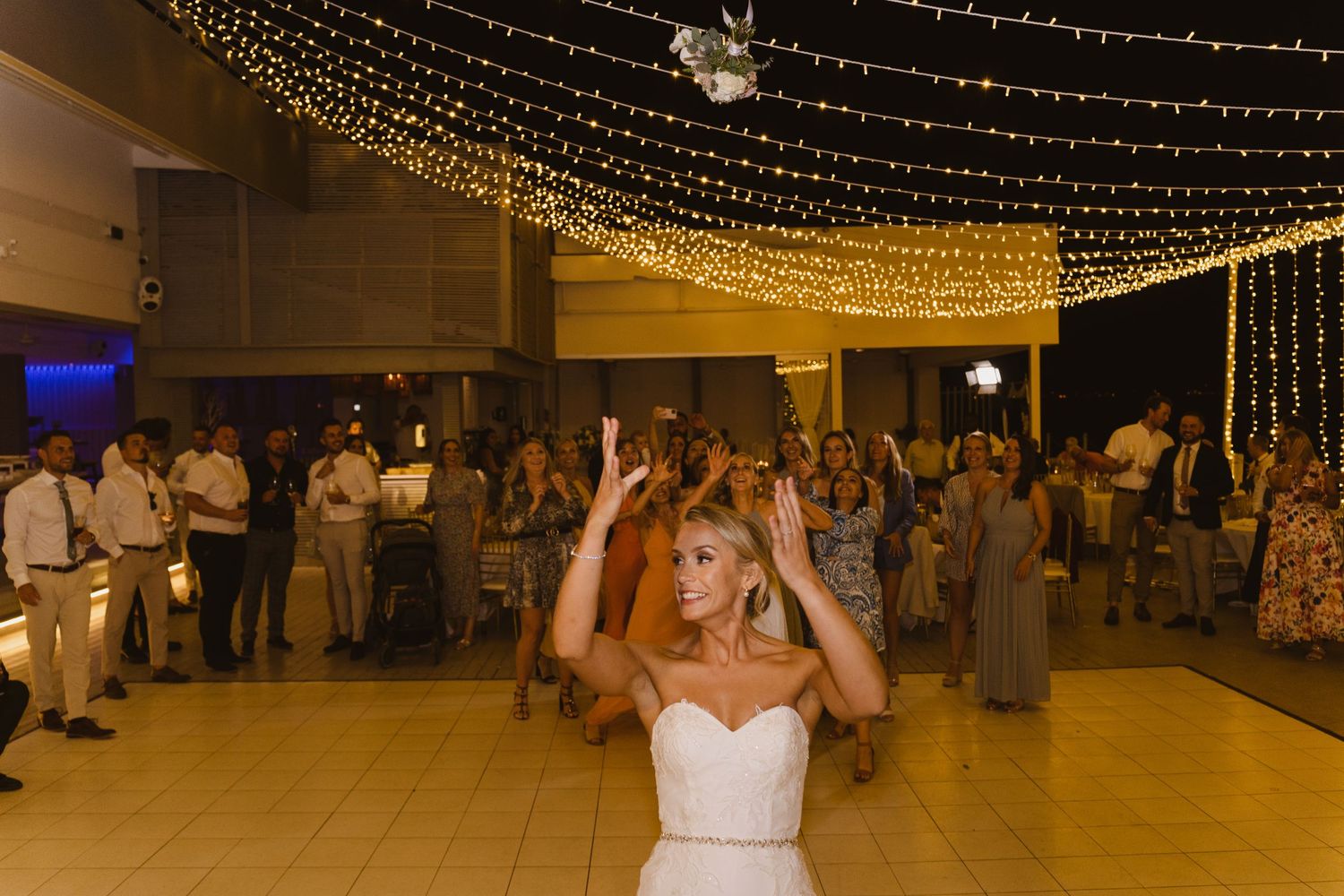 A wedding reception dance floor decorated with twinkling string lights overhead as guests celebrate.