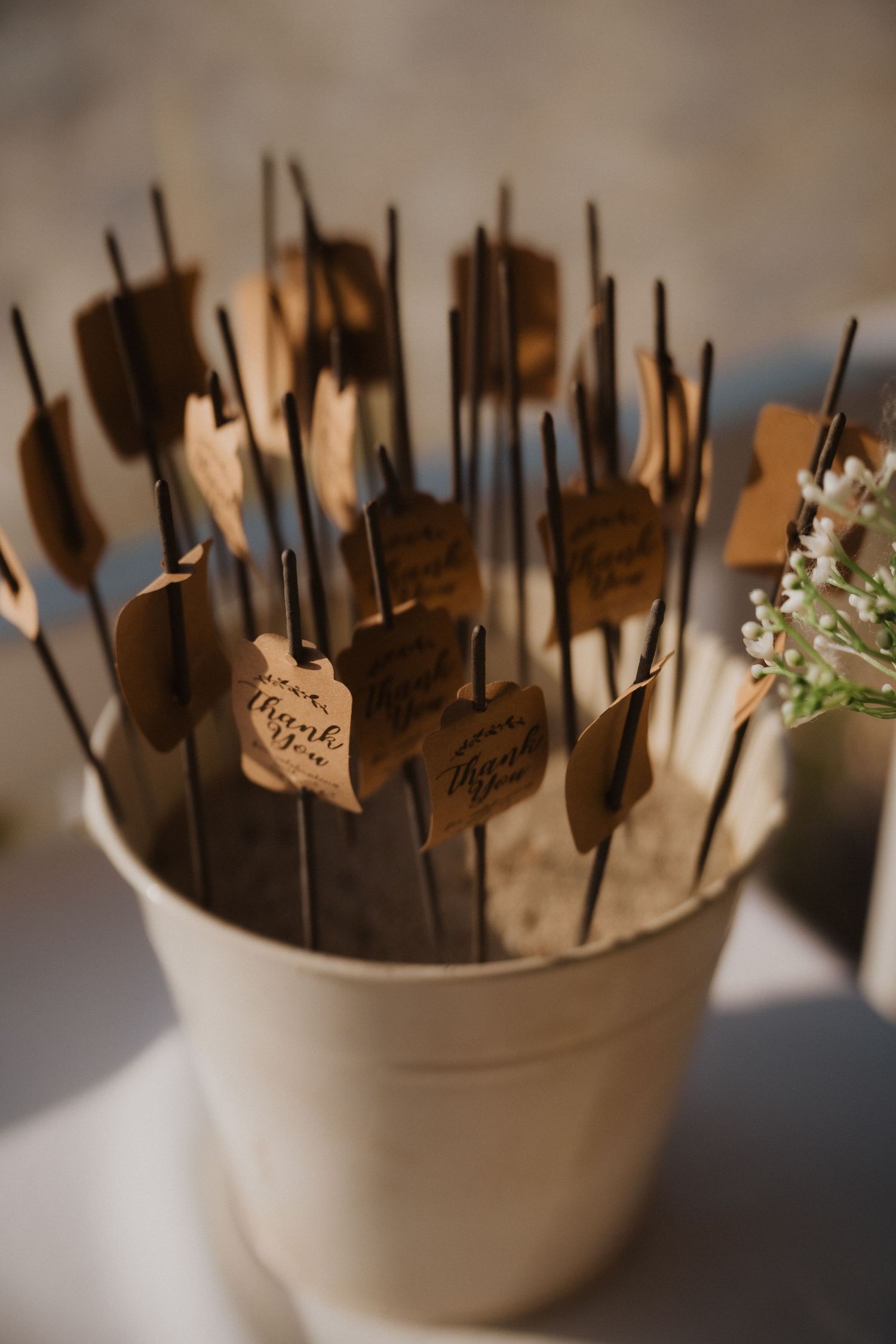 Wedding cake pops on sticks displayed in a white container with name tags attached.