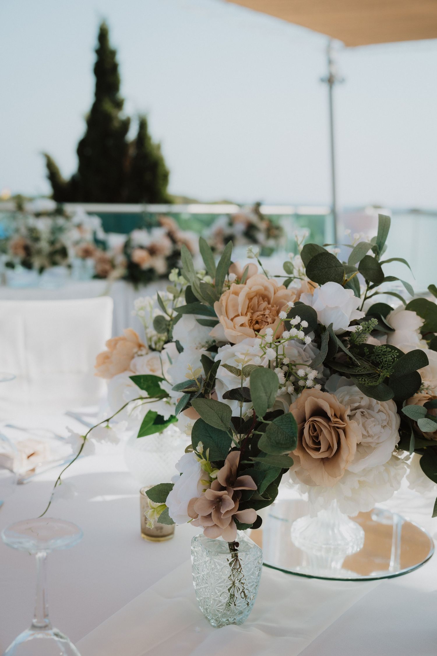 Wedding reception table with vintage glass vases holding peach and cream floral arrangements.
