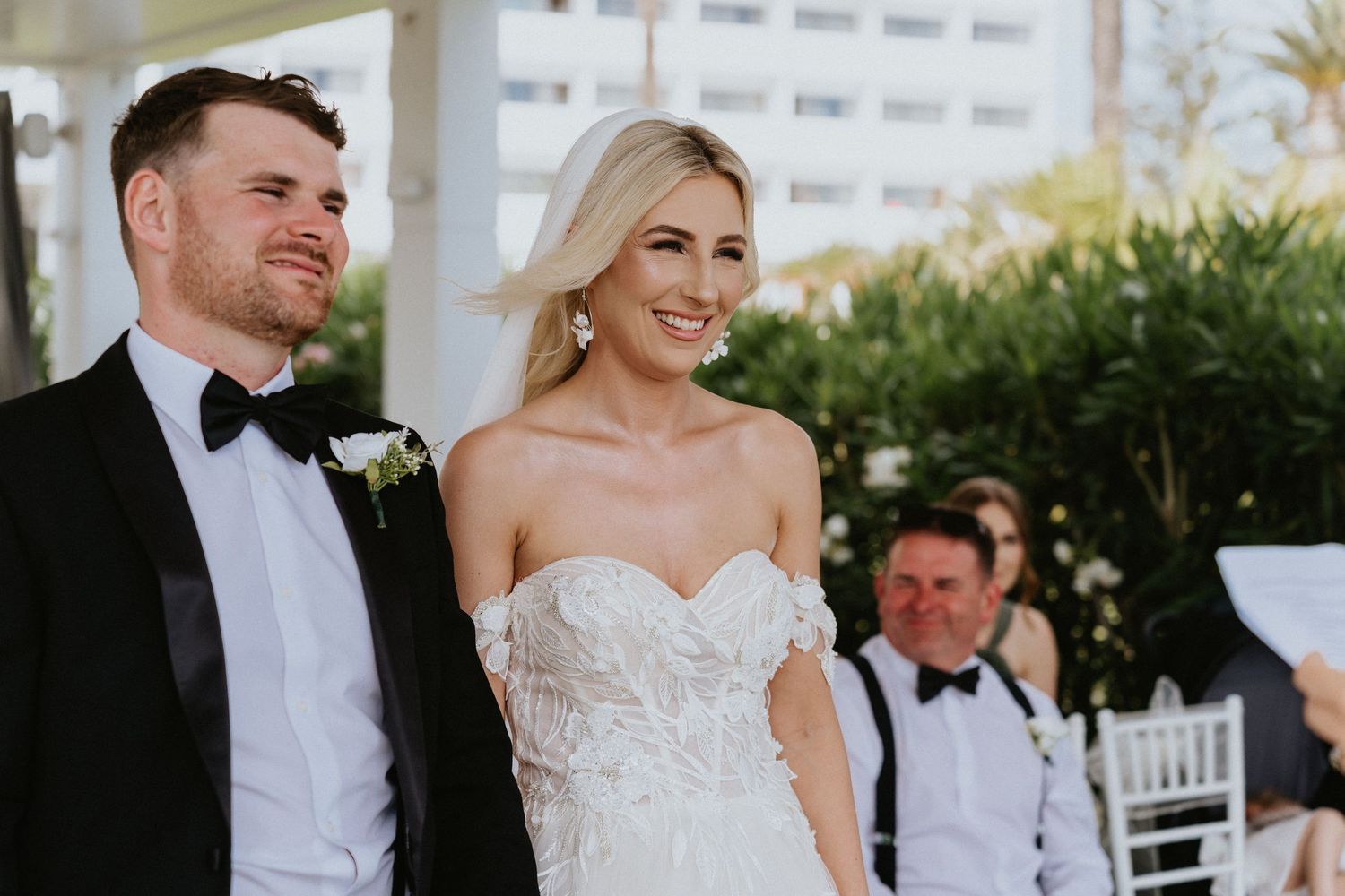Outdoor wedding ceremony with palm trees visible in background during an emotional moment.