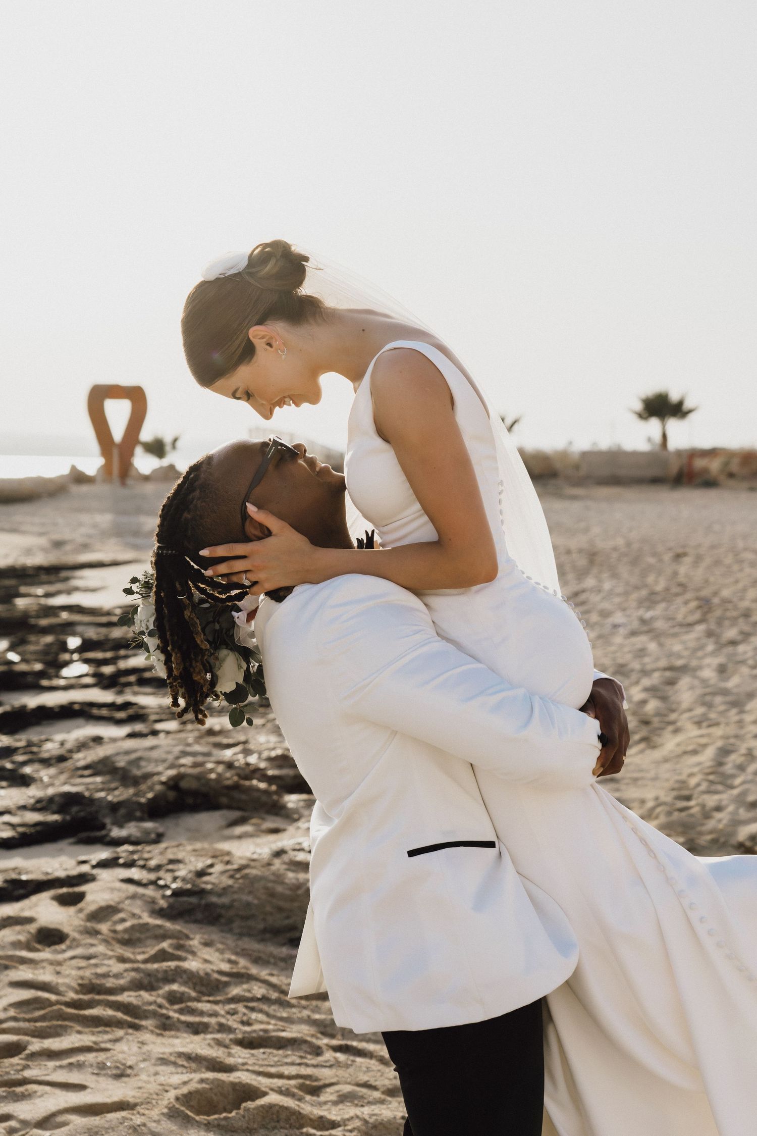 Intimate wedding moment captured on beach with couple in white and black attire.