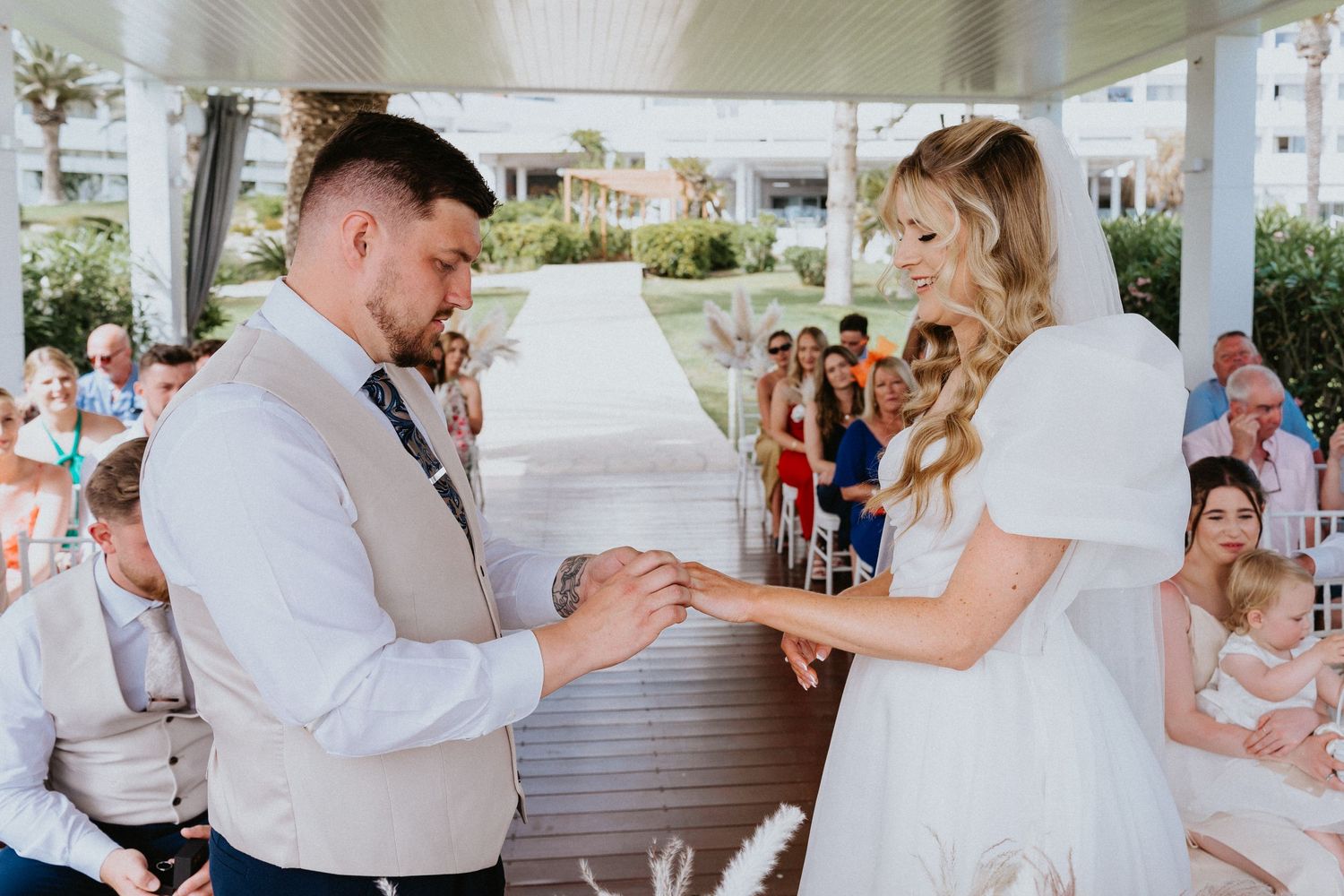 A wedding ceremony exchange of rings on an oceanfront deck decorated with pampas grass.