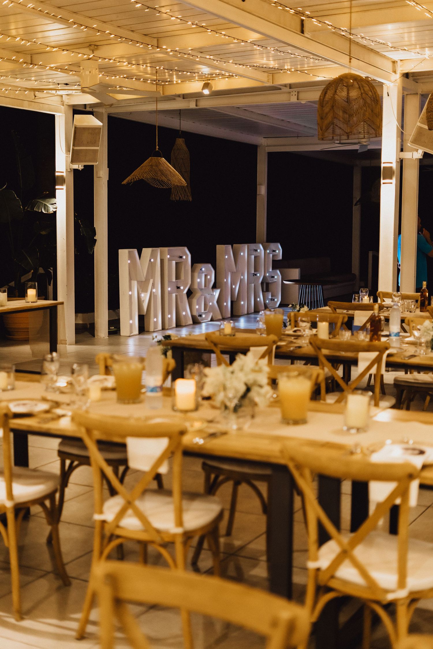 Wedding venue with illuminated MR&MRS sign and rustic table settings under twinkling lights.