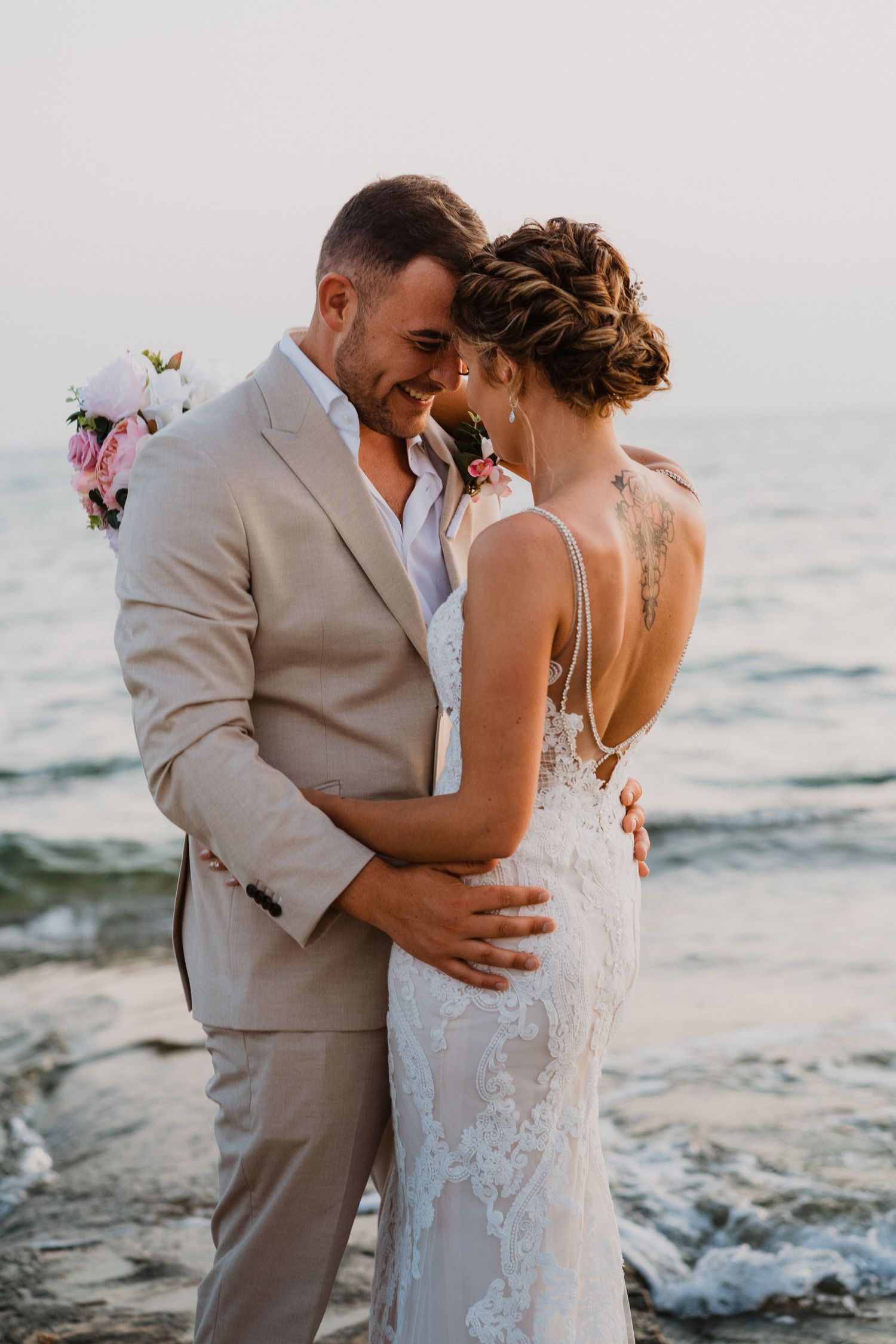 Romantic beachside wedding portrait with gentle ocean waves in the background at sunset.