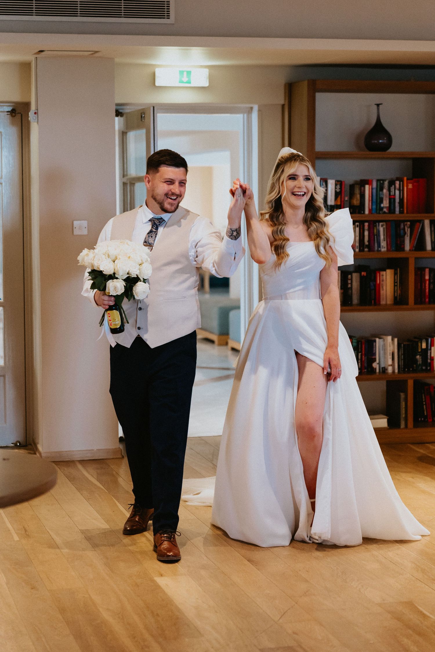Newlyweds make their grand entrance at their wedding reception with white roses and bookshelves in the background.