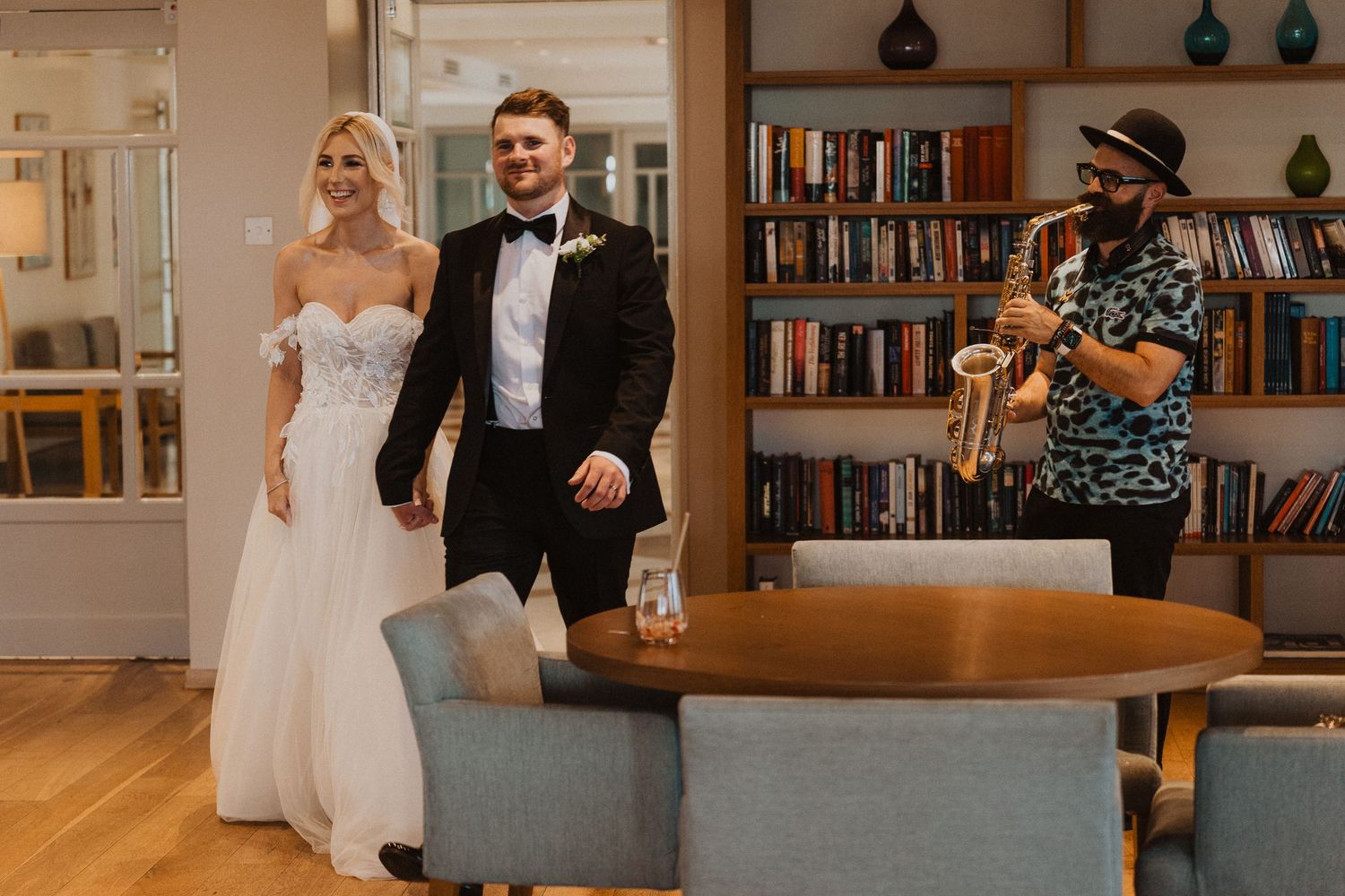 Wedding couple walks through modern library space during reception.
