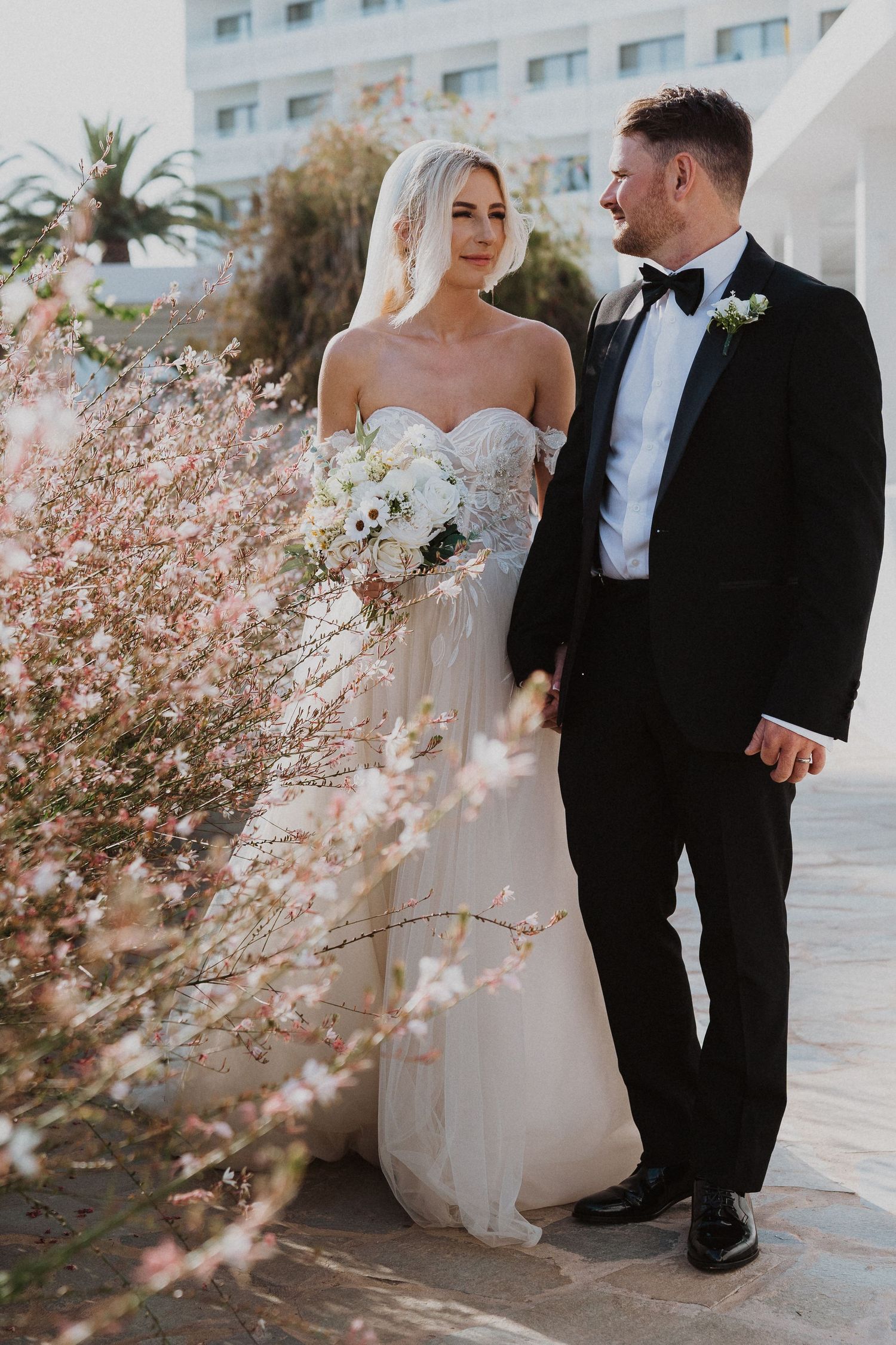Elegant wedding portrait with bride holding white bouquet against blooming spring flowers.