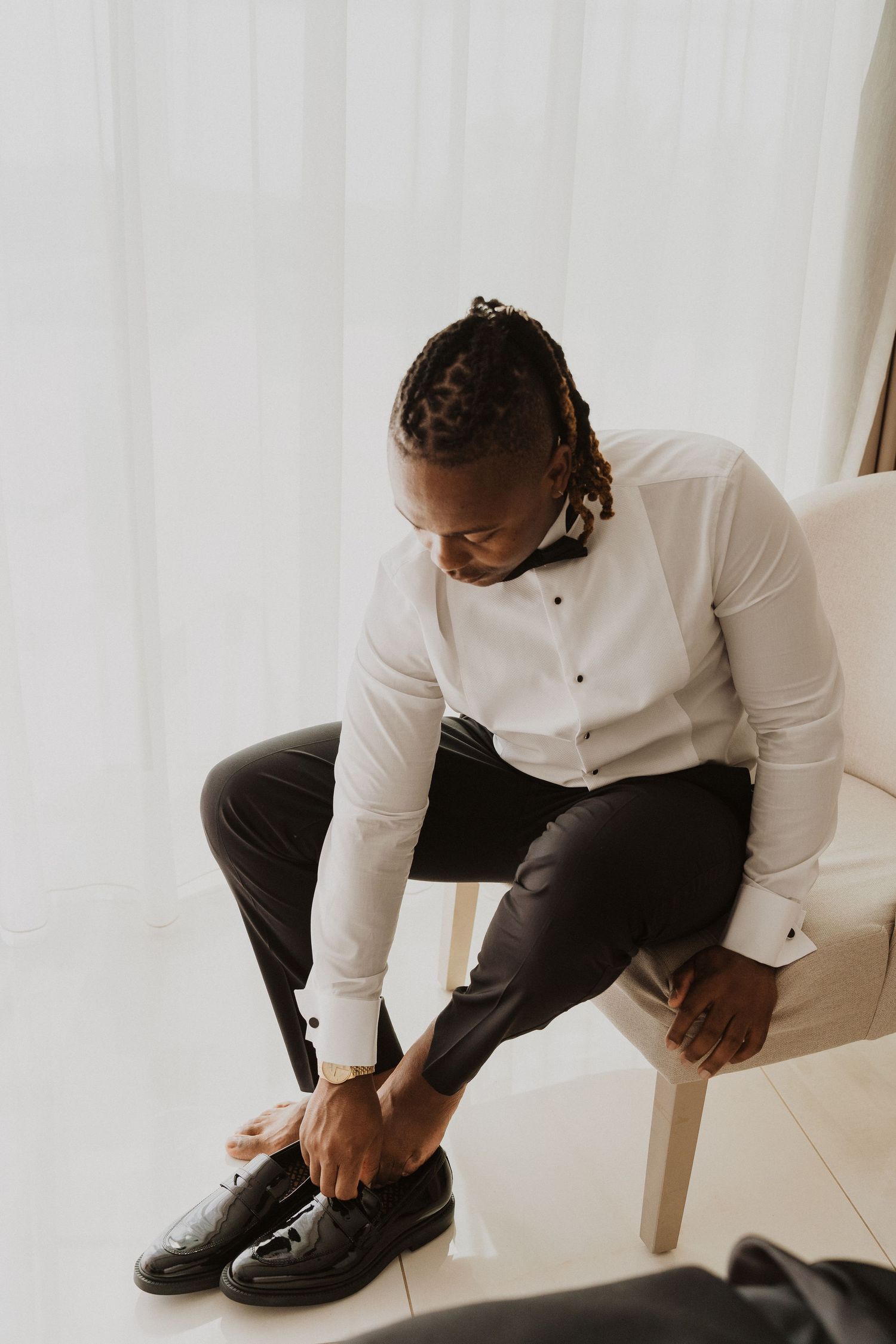 Person in formal white shirt and black pants putting on dress shoes while seated.