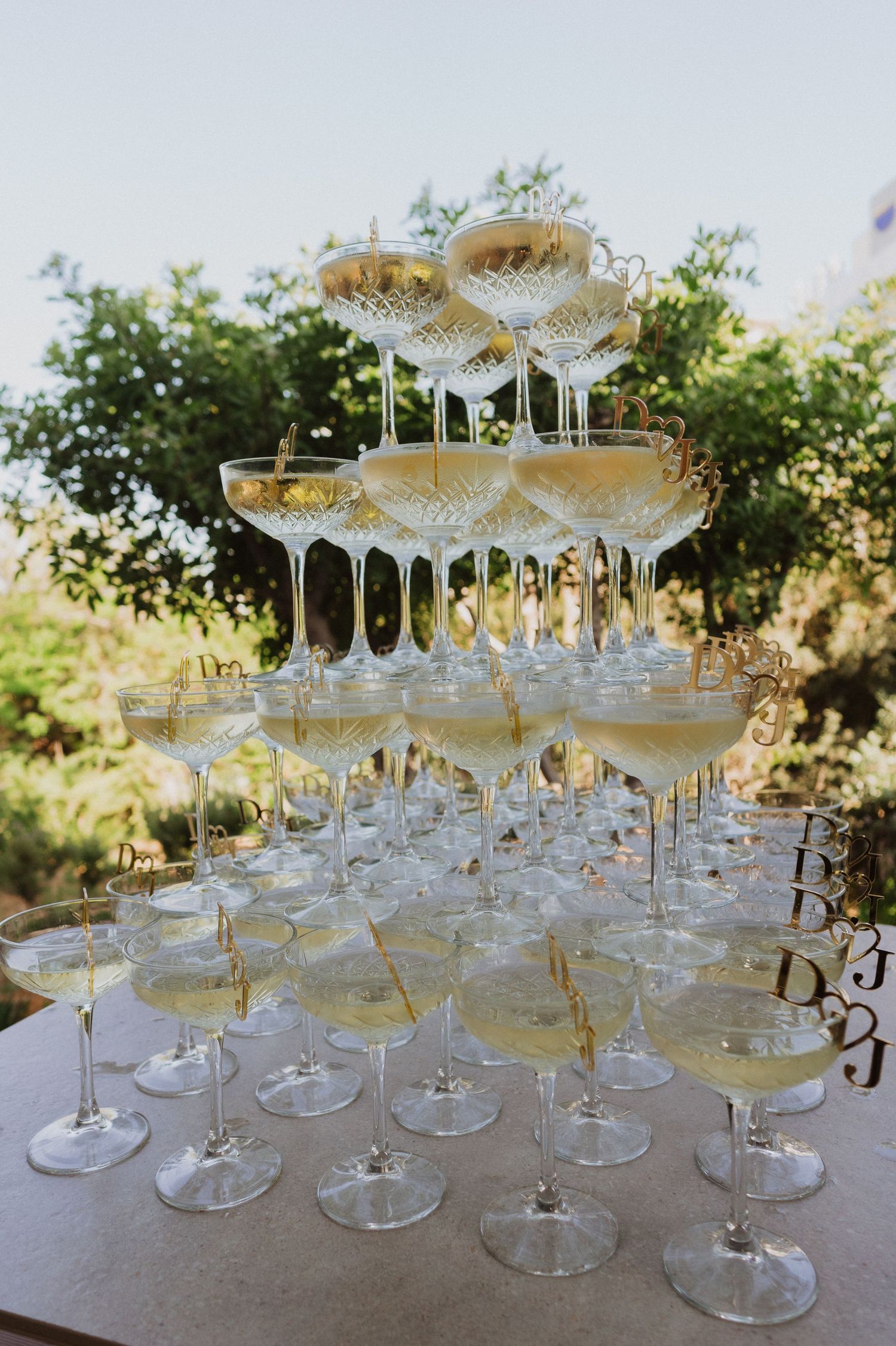 Elegant champagne tower setup with multiple tiers of coupe glasses arranged on a light-colored surface outdoors.