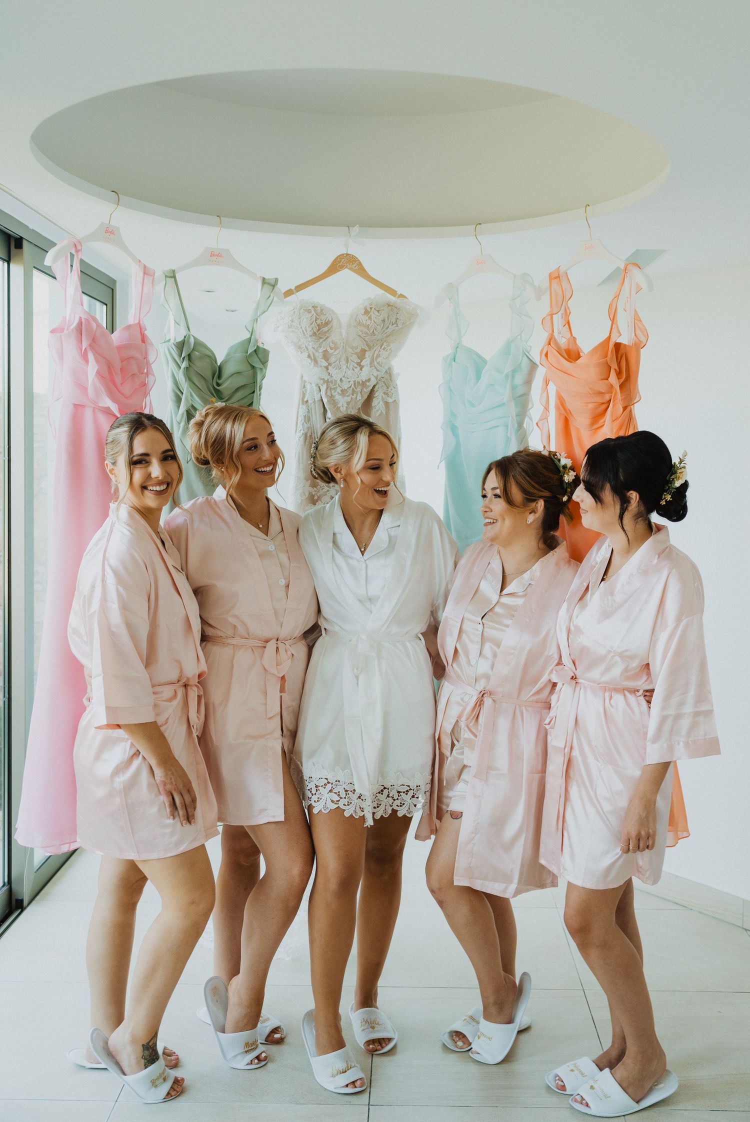 Bridesmaids in coordinated pink robes and slippers pose together before the wedding ceremony.