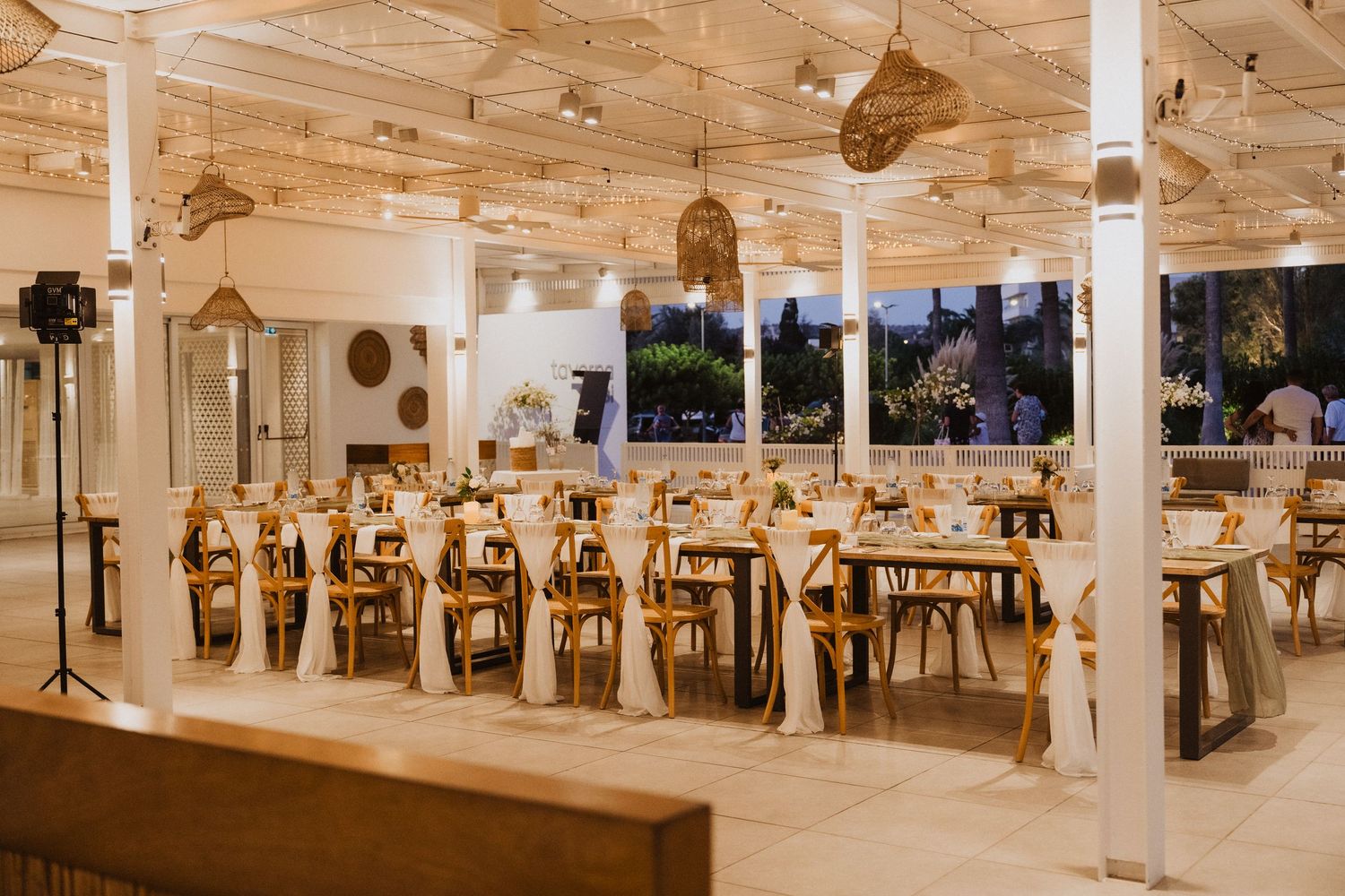 Evening wedding reception venue with wooden tables and hanging wicker light fixtures.