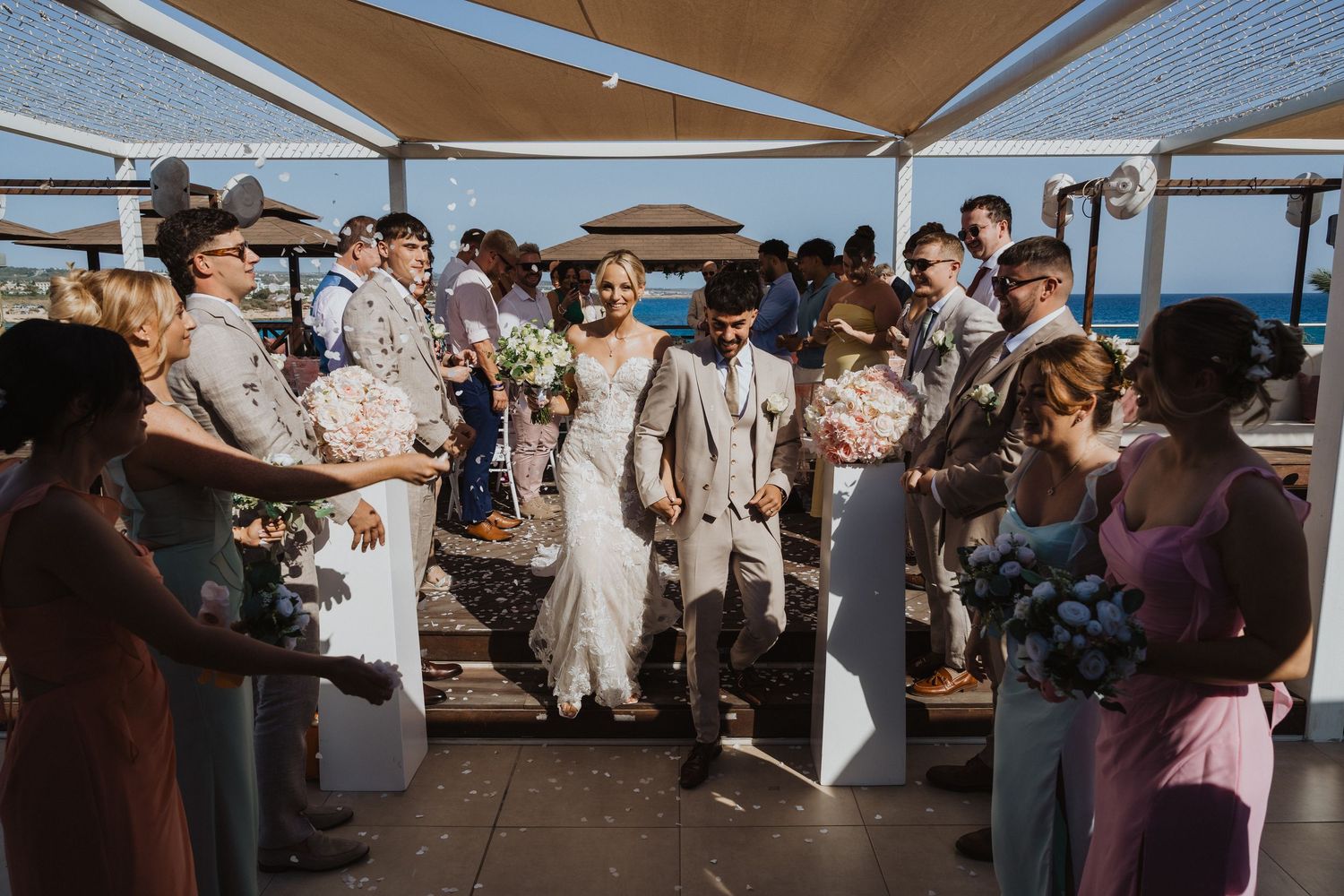 Wedding party gathered on a covered outdoor terrace with ocean views in the background.