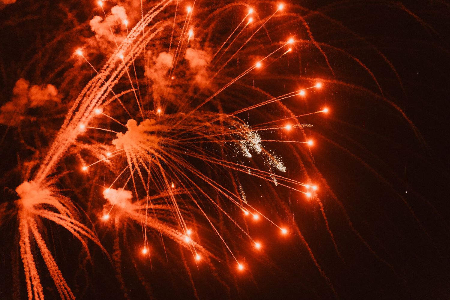 Close-up shots of bright red fireworks bursting in a starlike pattern against black sky.