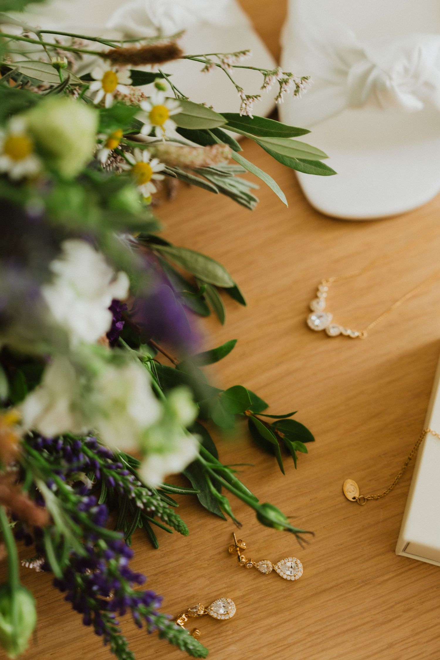 Wedding jewelry and floral arrangements with purple accents displayed on wooden table.