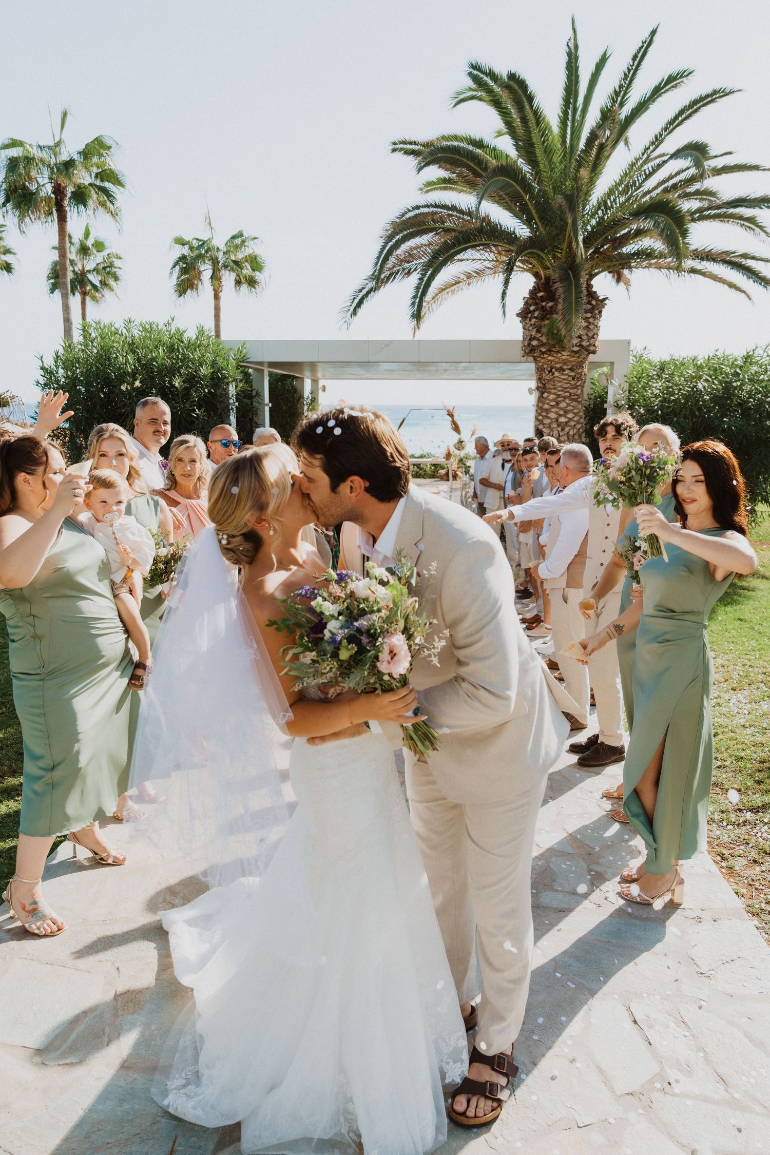 Festive wedding exit with confetti shower and tropical palm trees in the background.