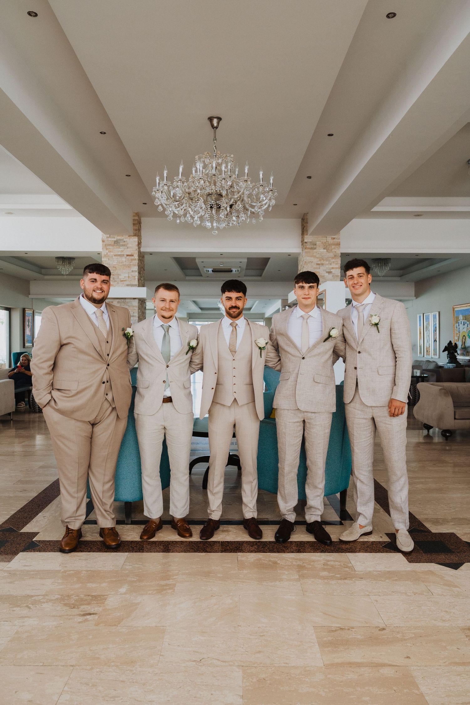 Groomsmen group photo in light tan suits standing against turquoise accent wall.