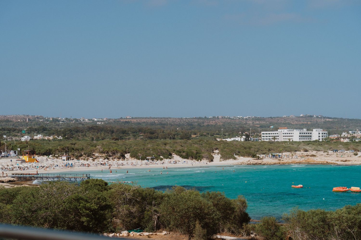 Panoramic view of a coastal town with turquoise waters, boats, and buildings along the shoreline.