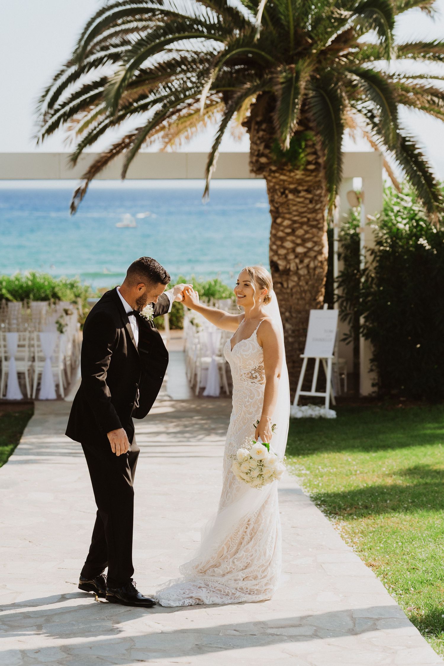 A couple shares a romantic moment during their beach wedding ceremony with palm trees and ocean views in the background.