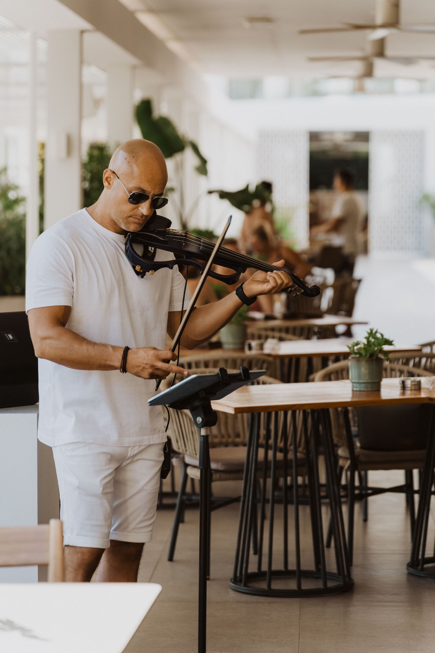 A musician performs on violin in a modern restaurant space with white columns and dark tables in the background.