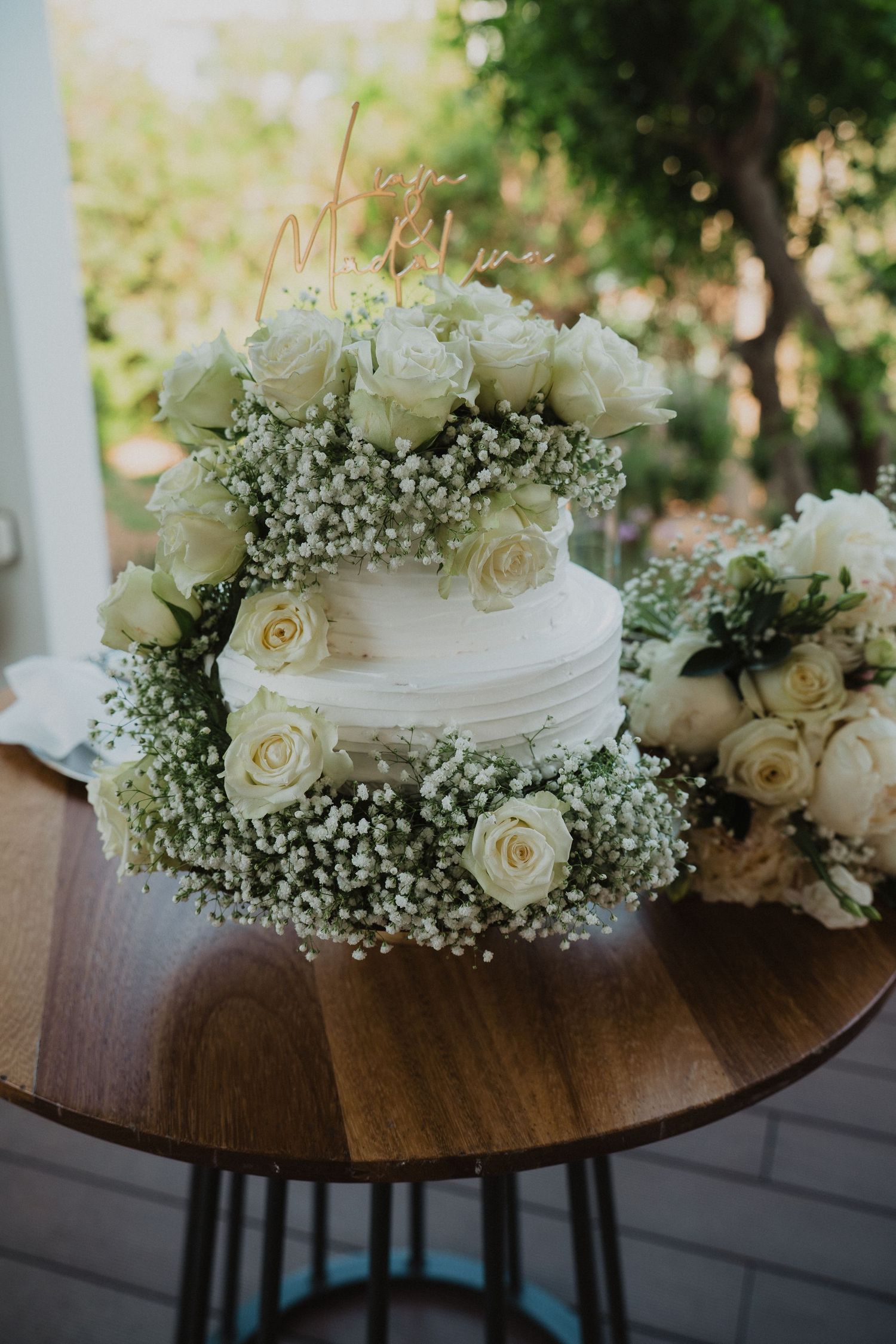Elegant two-tier white wedding cake decorated with white roses and baby's breath on a wooden table.