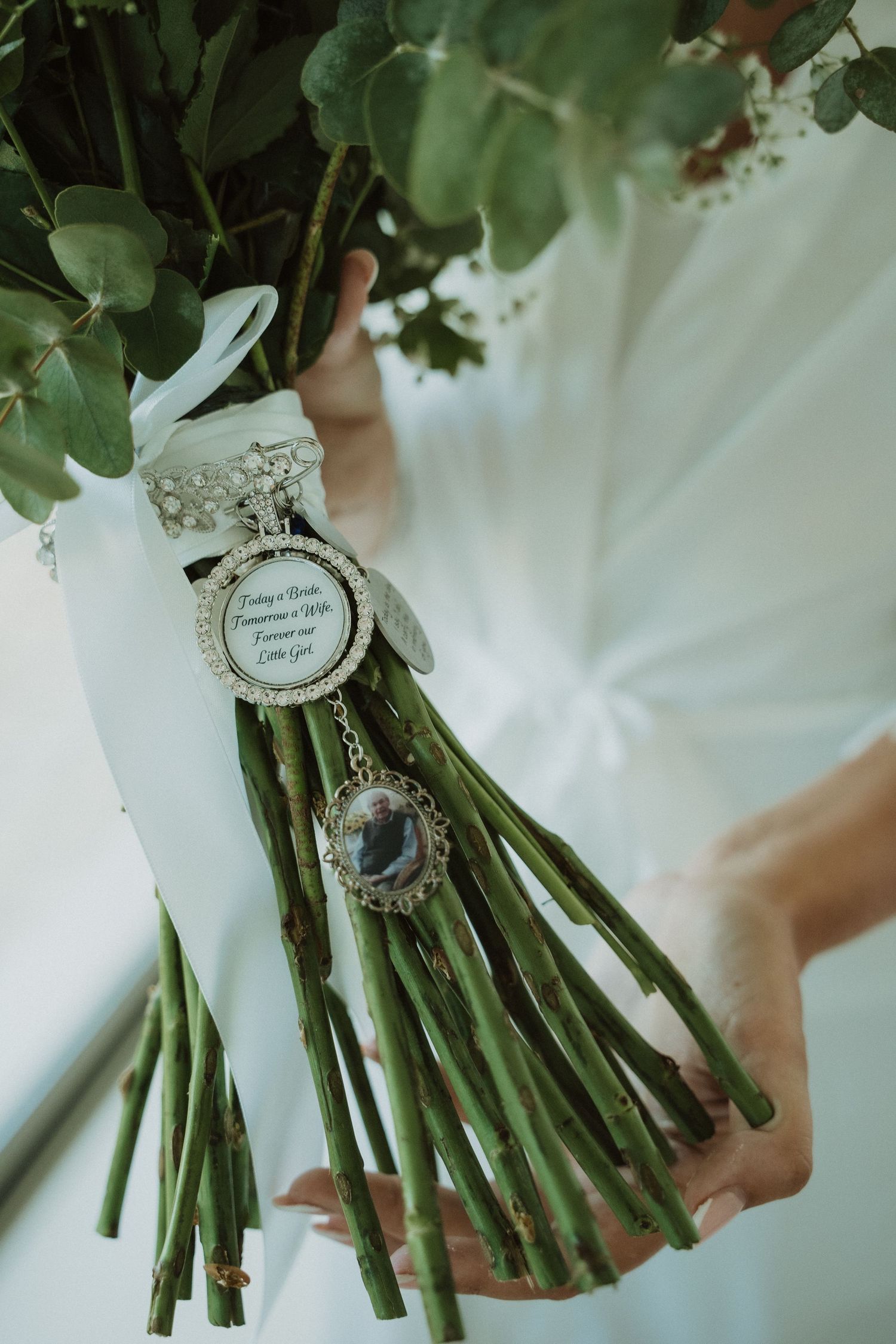 A bridal bouquet wrapped in white ribbon features a sentimental charm or locket tied to the stems.