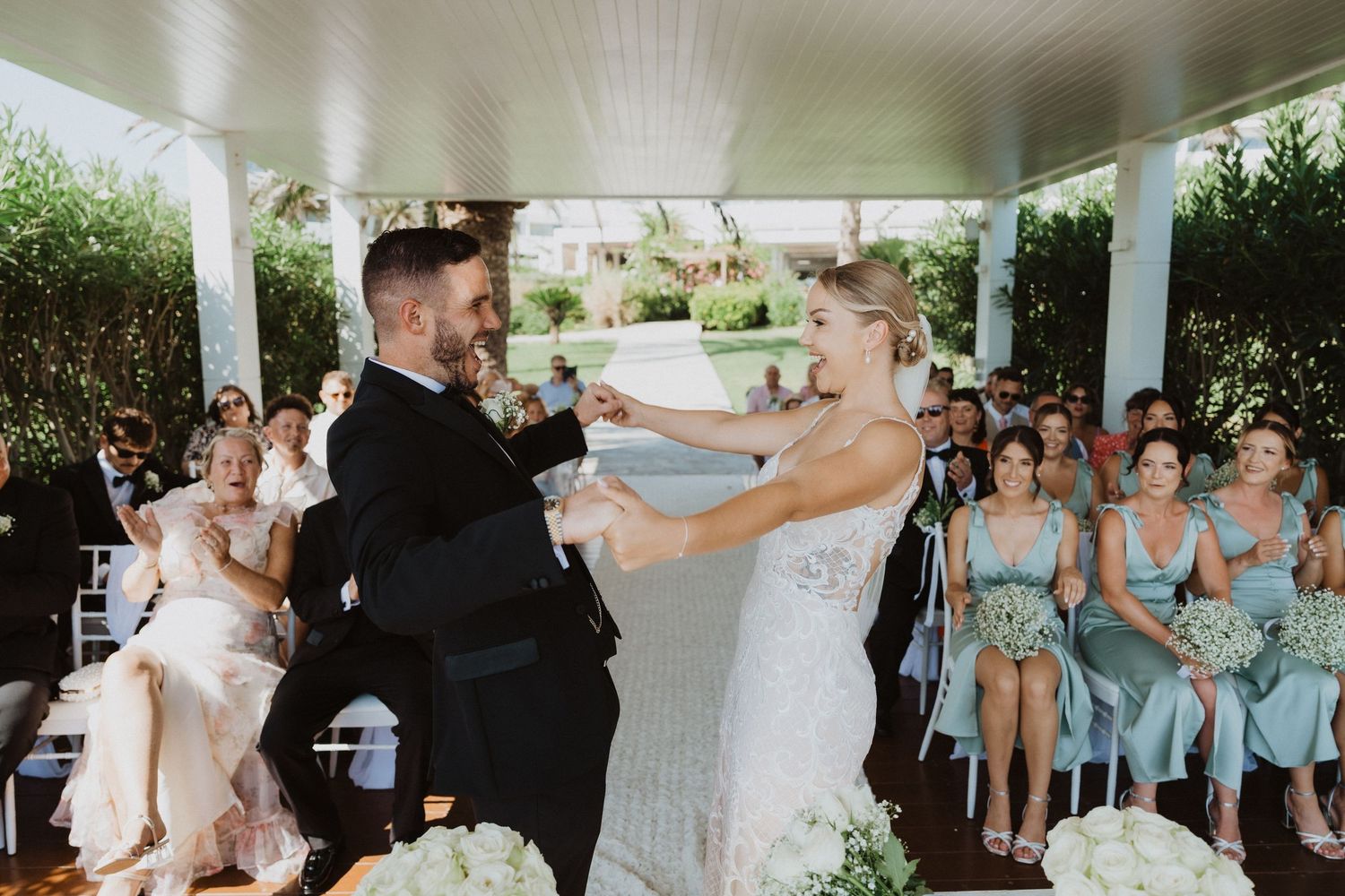 Newlyweds celebrate during ceremony with bridesmaids in mint dresses watching.