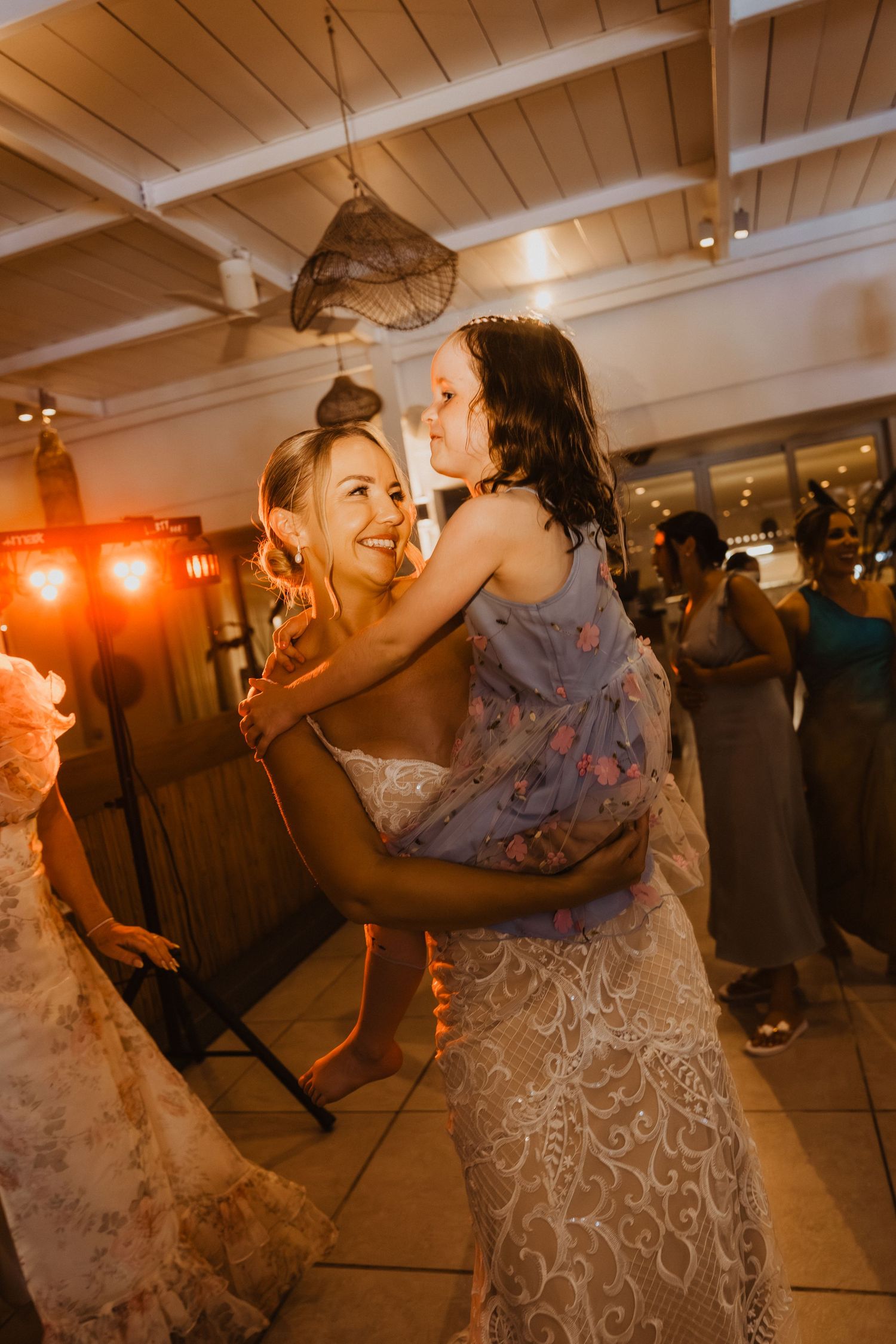 Wedding guests dancing together in a lively reception venue with wooden ceiling beams and warm lighting.