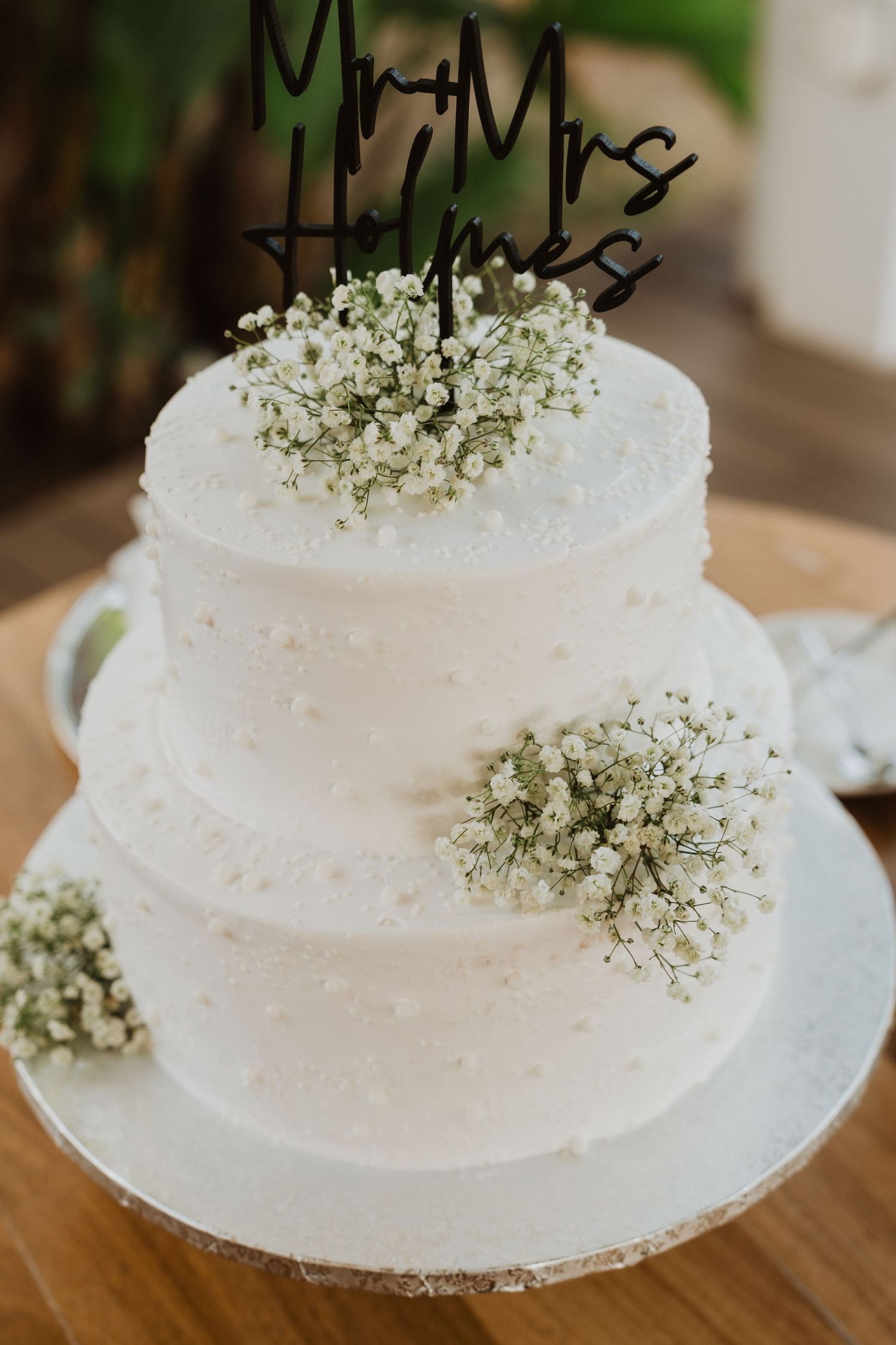 Elegant white wedding cake decorated with delicate baby's breath flowers on a wooden table.