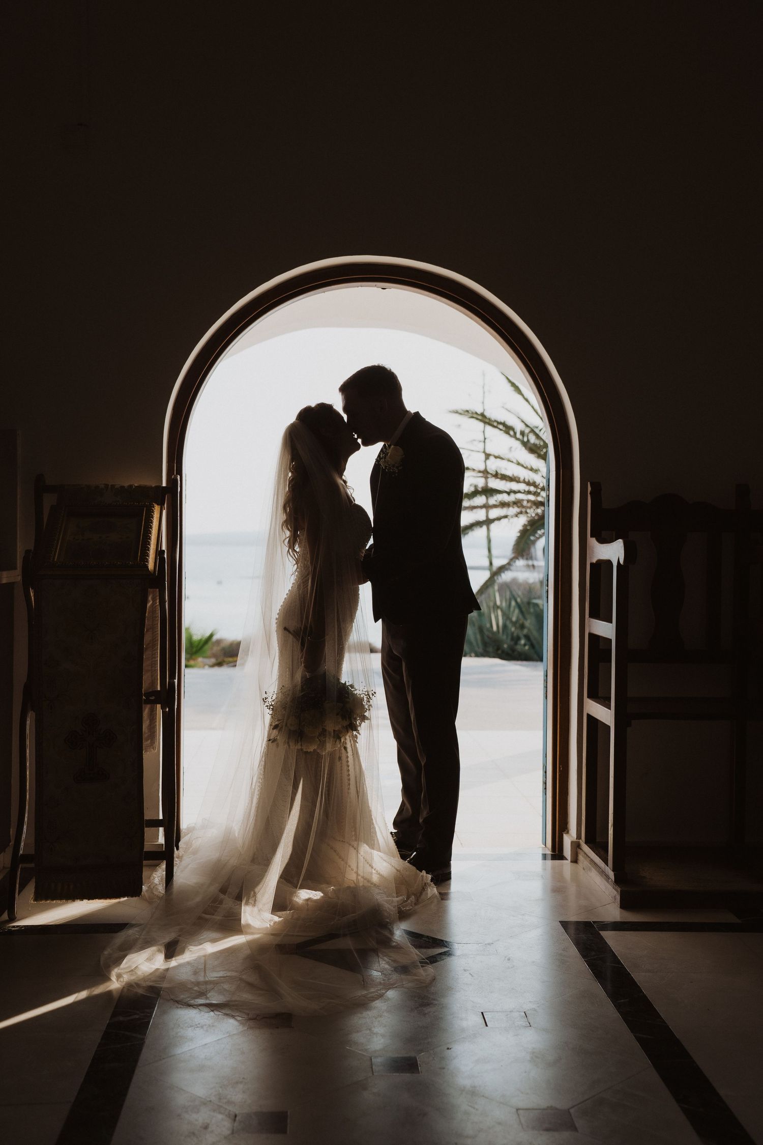 Silhouette of bride and groom sharing a tender moment in an arched doorway with ocean views behind them.