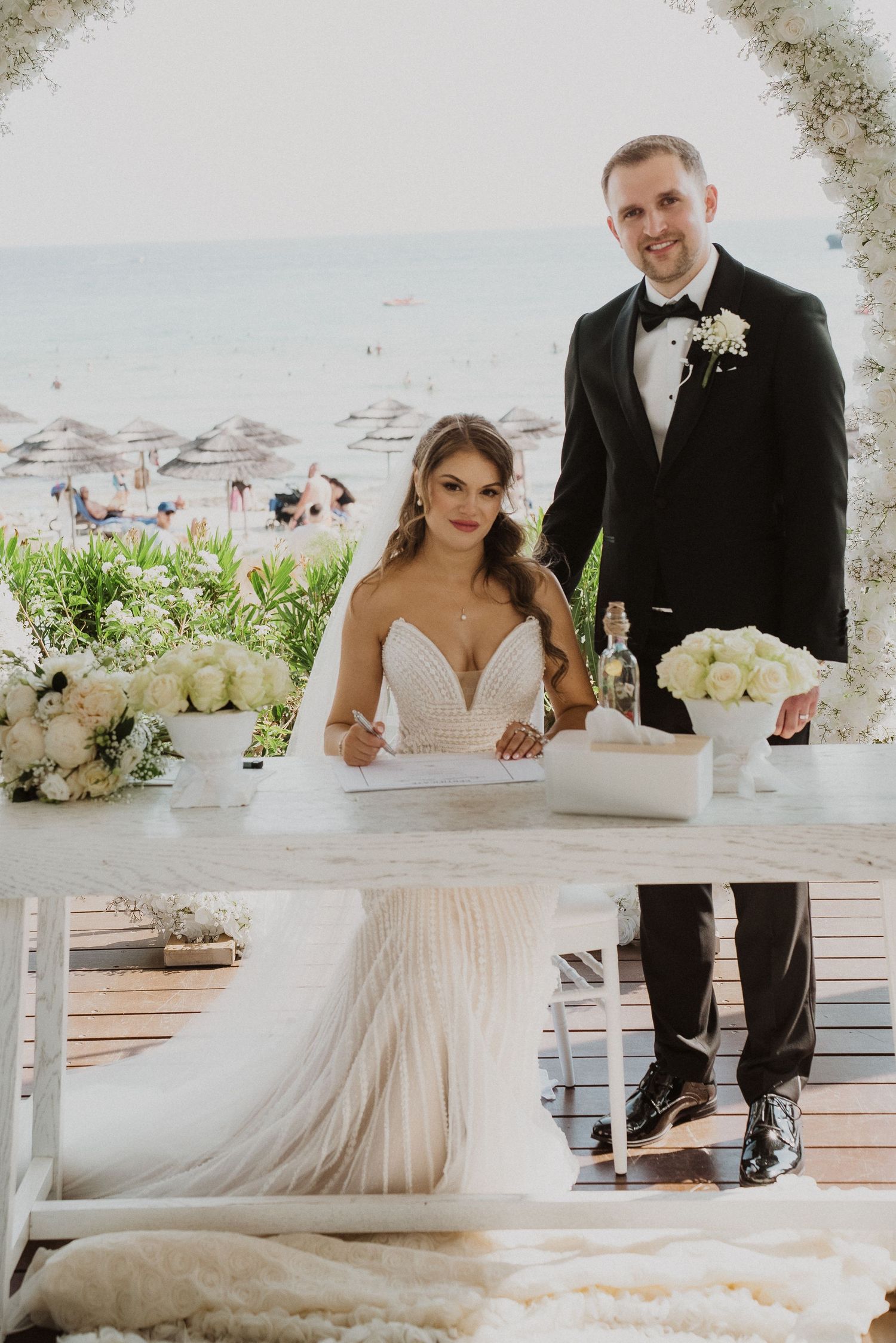 Bride and groom signing marriage certificate at beachside wedding ceremony table.
