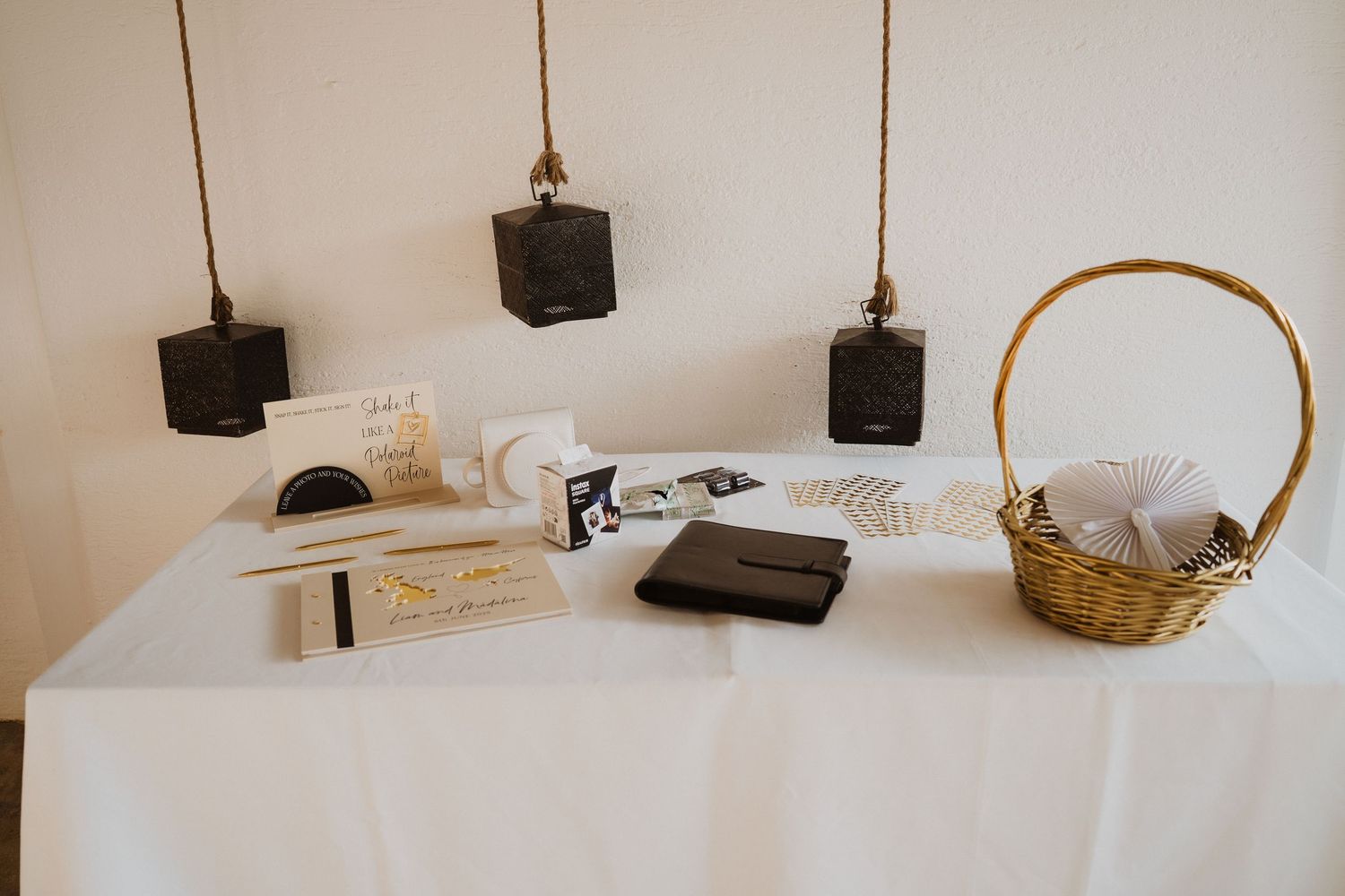 Elegant wedding gift table with white linen, wicker basket, stationery, and hanging black pendant lights.