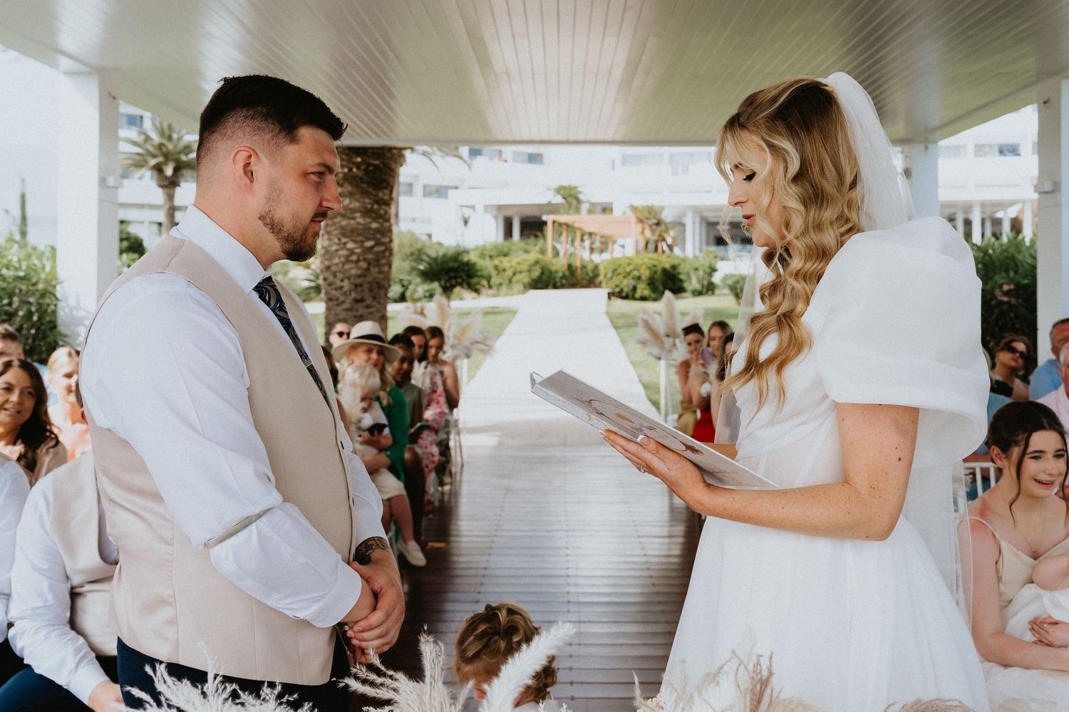 Couple reads vows during intimate outdoor ceremony surrounded by tropical landscaping.