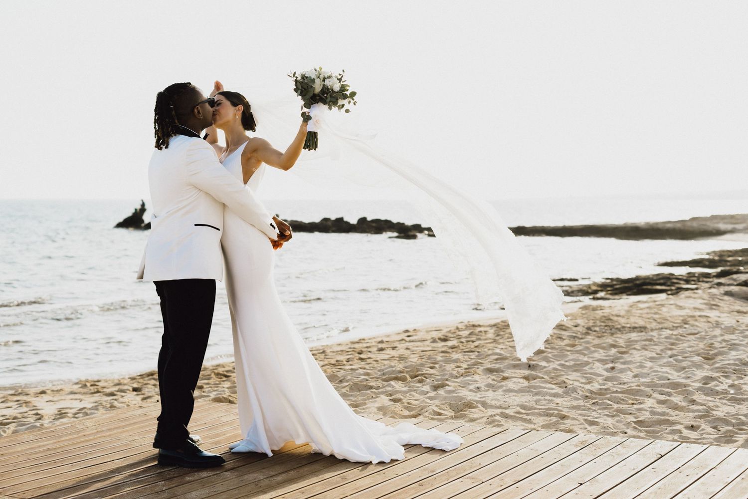 A wedding couple embraces on a beach boardwalk with the ocean in the background.