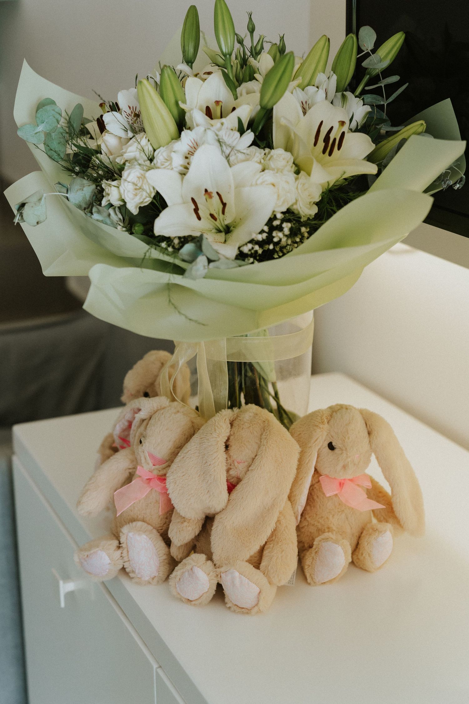 White lily bouquet with plush bunny toys sitting on white furniture.