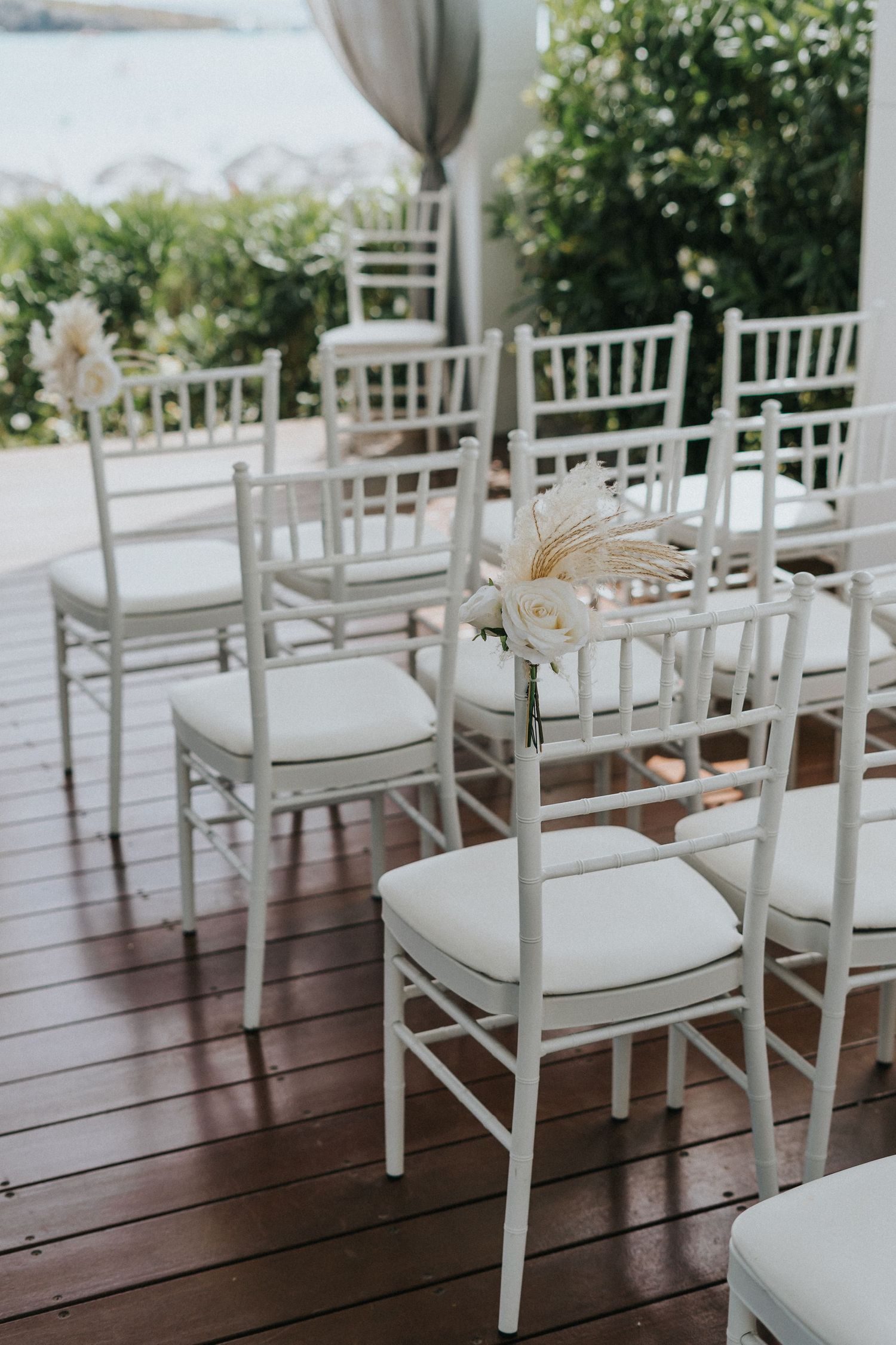 White Chiavari chairs arranged for a beach wedding ceremony on a wooden deck.