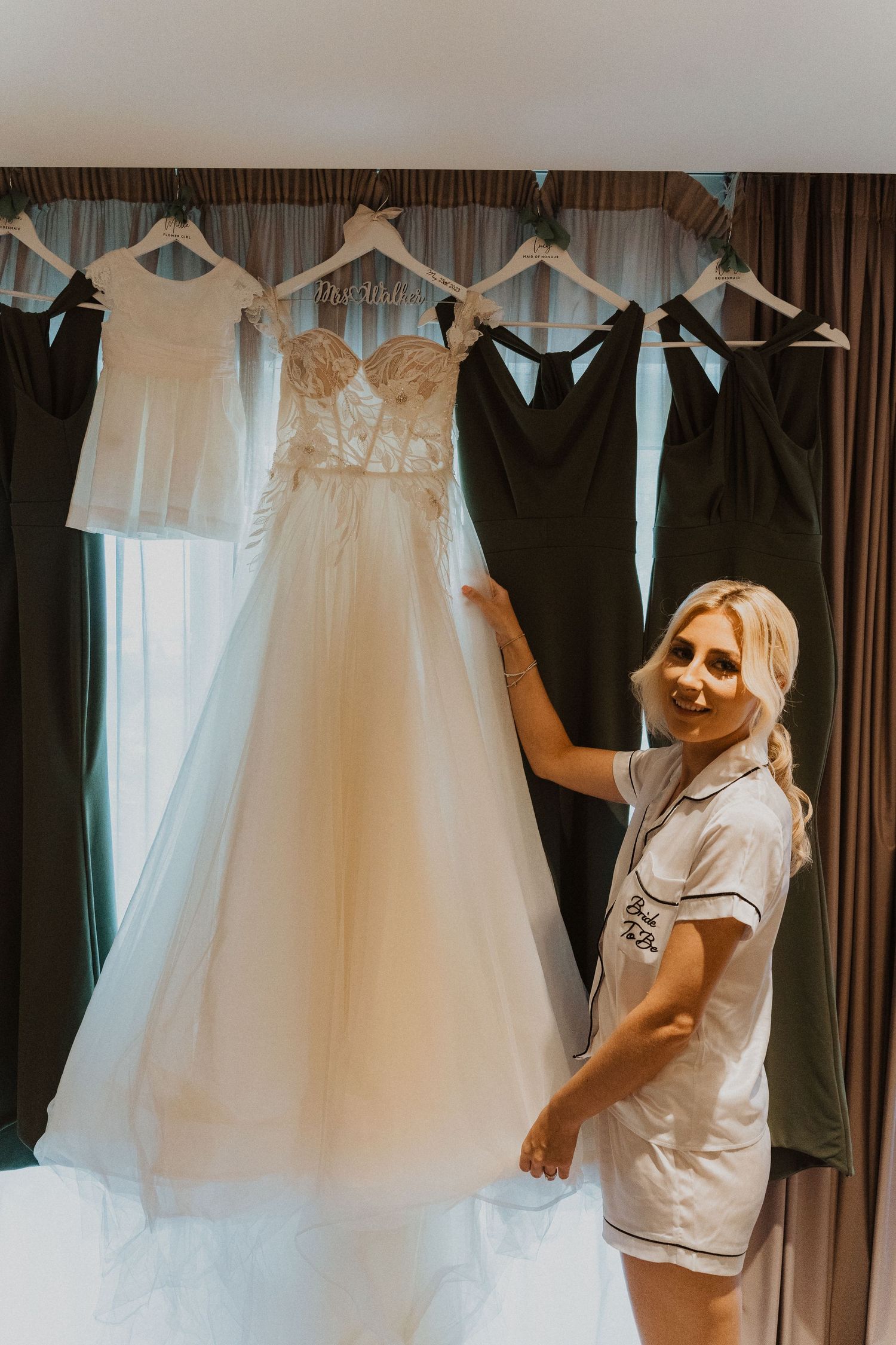 A display of wedding attire including a white bridal gown and dark bridesmaid dresses on hangers.
