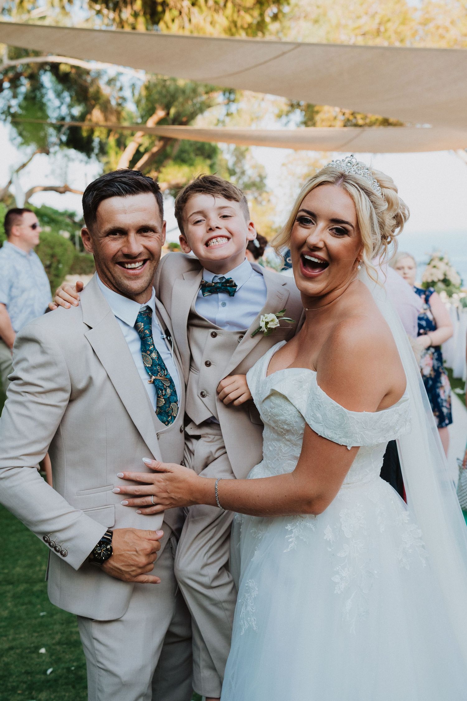 A joyful wedding celebration outdoors with a bride in white and wedding party wearing light beige suits.
