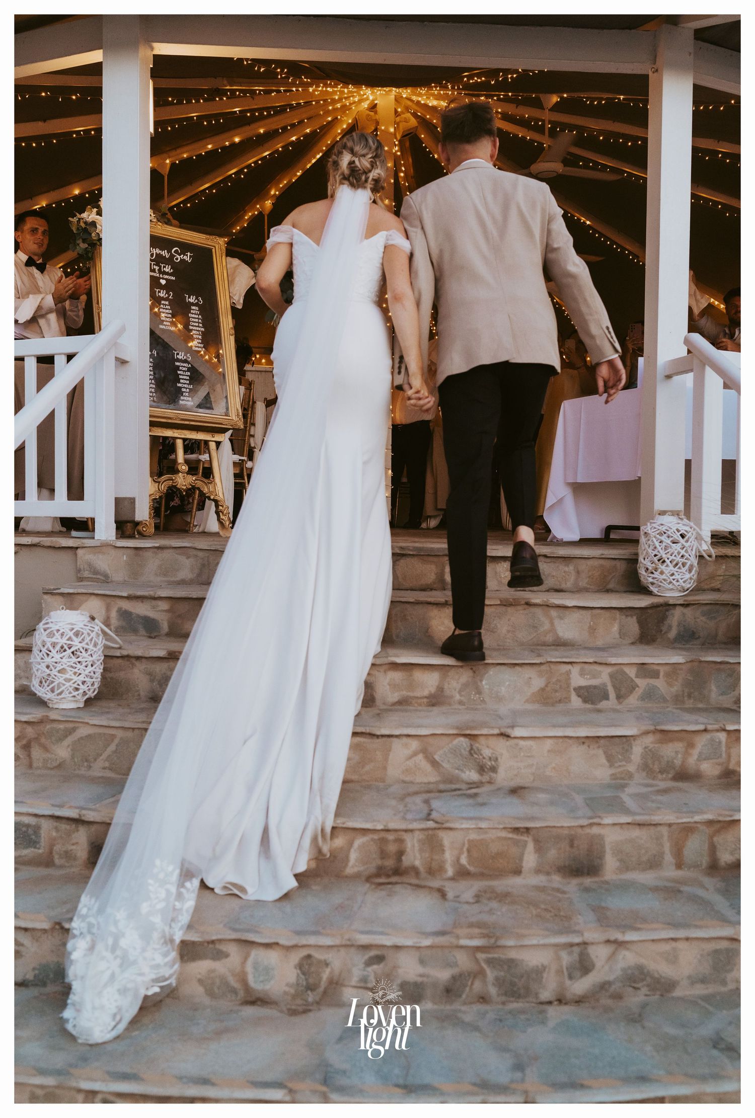 Couple ascending stone steps under string lights at evening wedding reception.