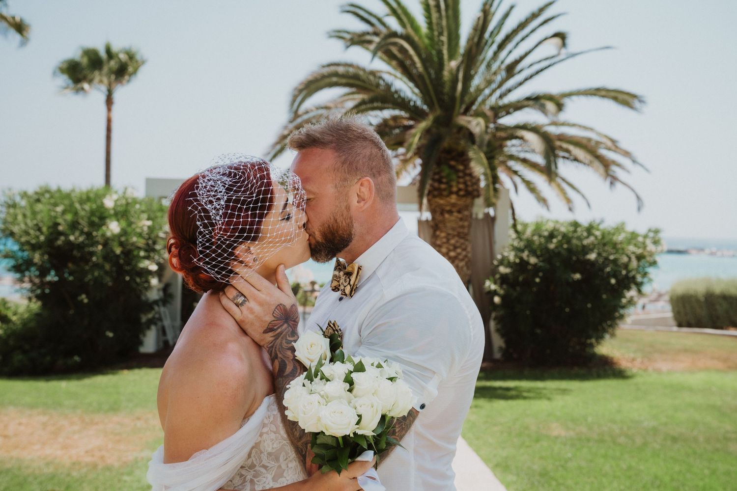 Close-up beach wedding portrait with palm trees and ocean in soft focus background.