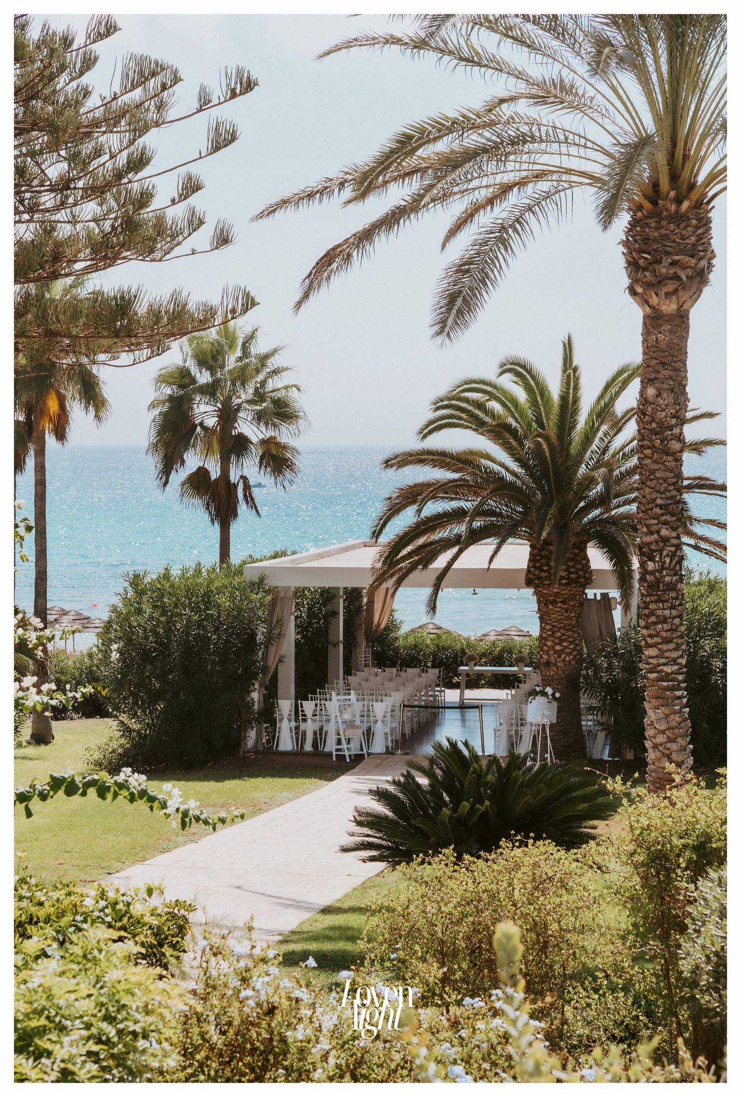 Beachfront wedding venue with palm trees and a white gazebo overlooking the ocean.